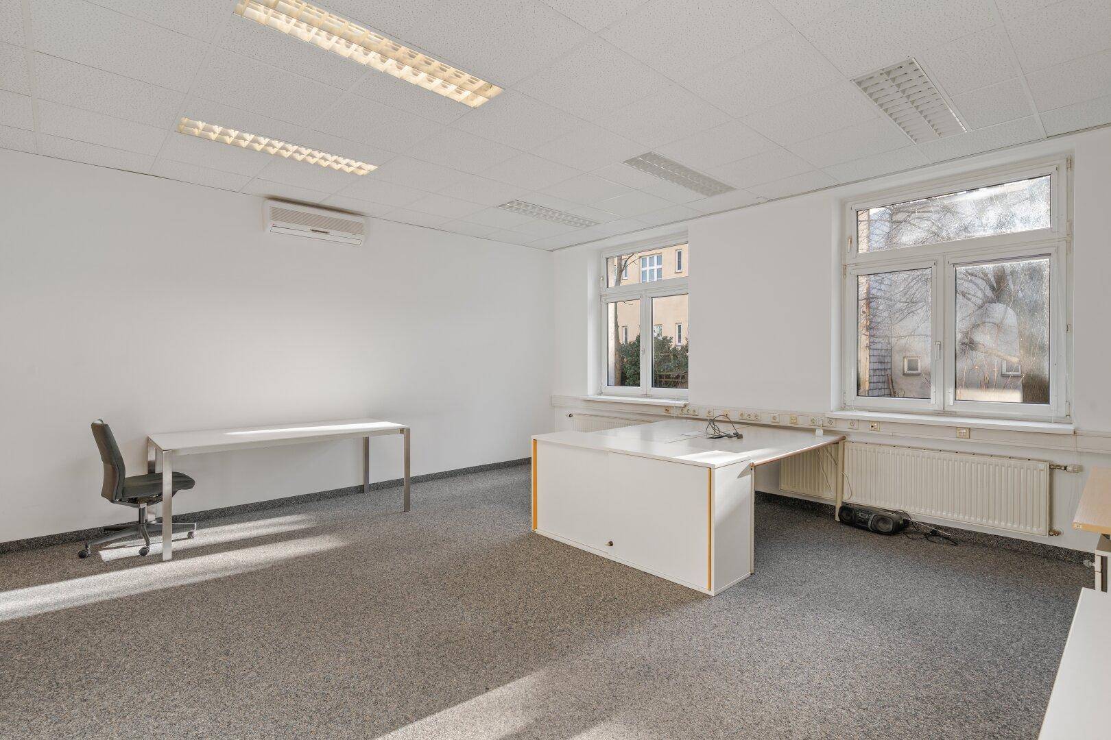 Modernes Büro mit Teppichboden, Klimaanlage und großen Fenstern, ausgestattet mit einem Schreibtisch und Stuhl.