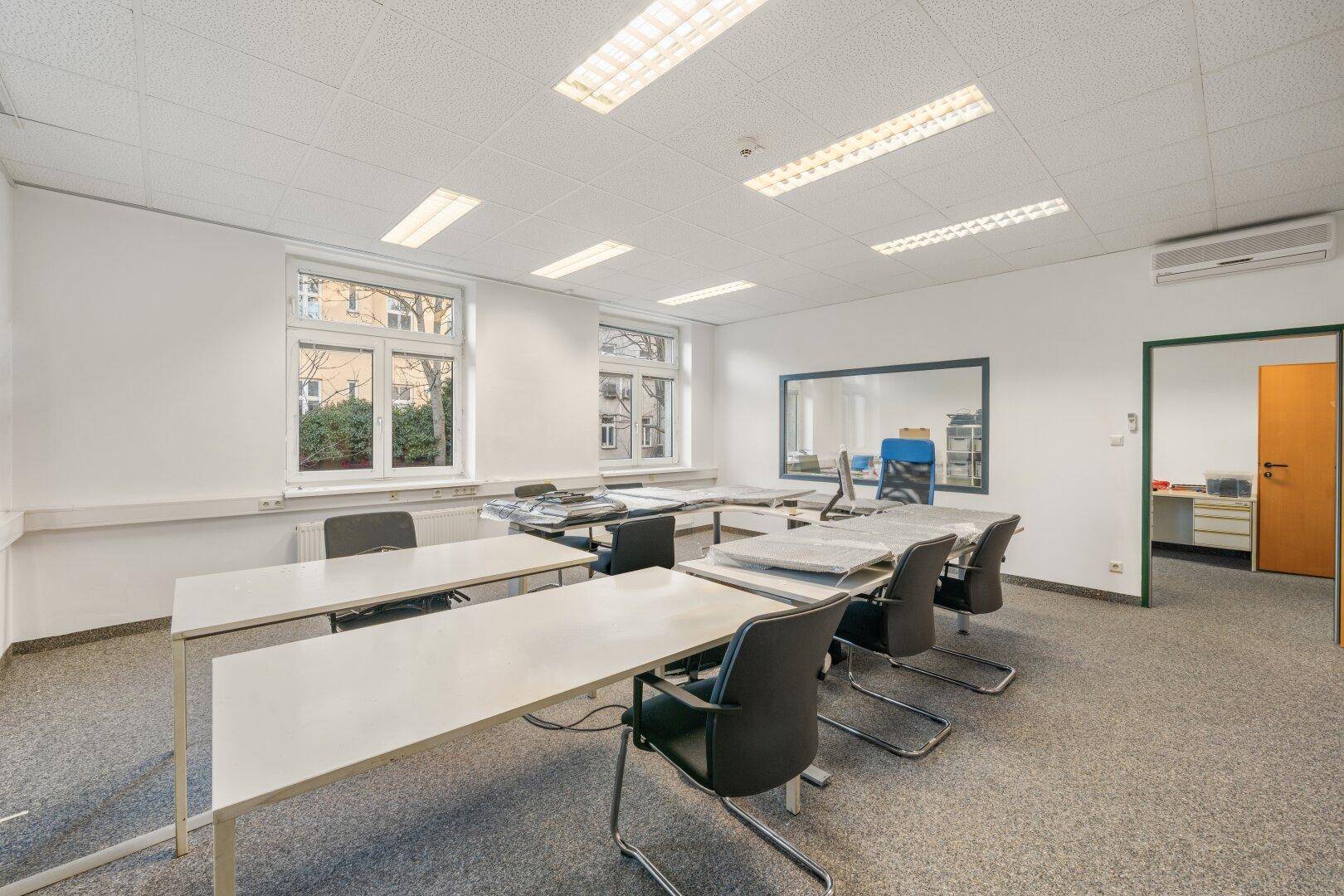 Großes Büro mit flexiblen Arbeitsplätzen, Klimaanlage und einem Fenster zum angrenzenden Raum.