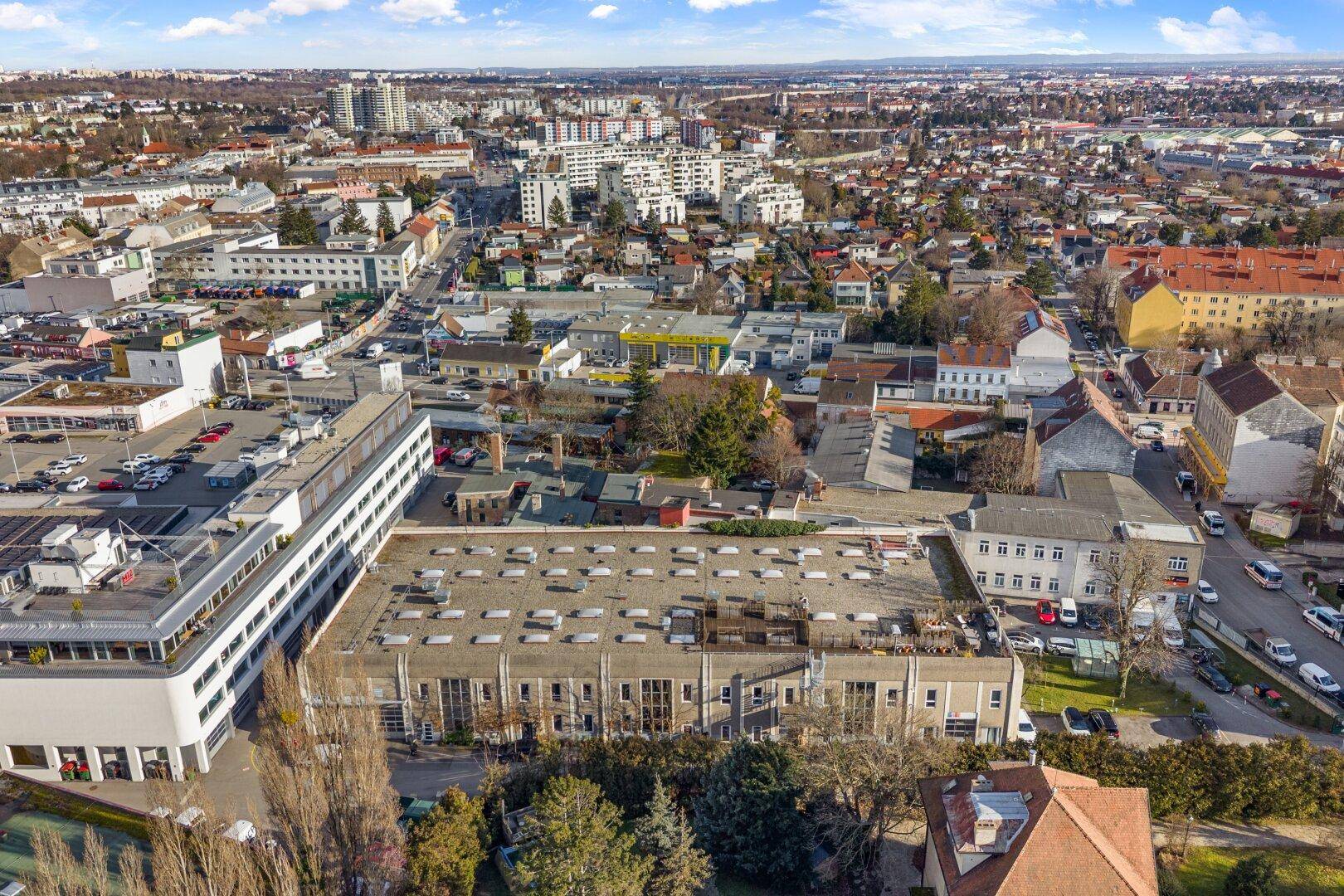 Luftaufnahme eines großen Gebäudekomplexes in einer städtischen Umgebung mit umliegenden Wohngebäuden.