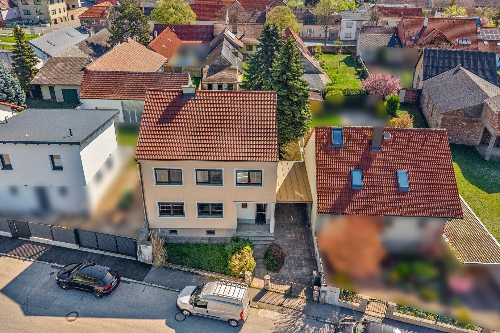 Luftaufnahme des Hauses von vorne mit Straße und benachbarten Gebäuden.