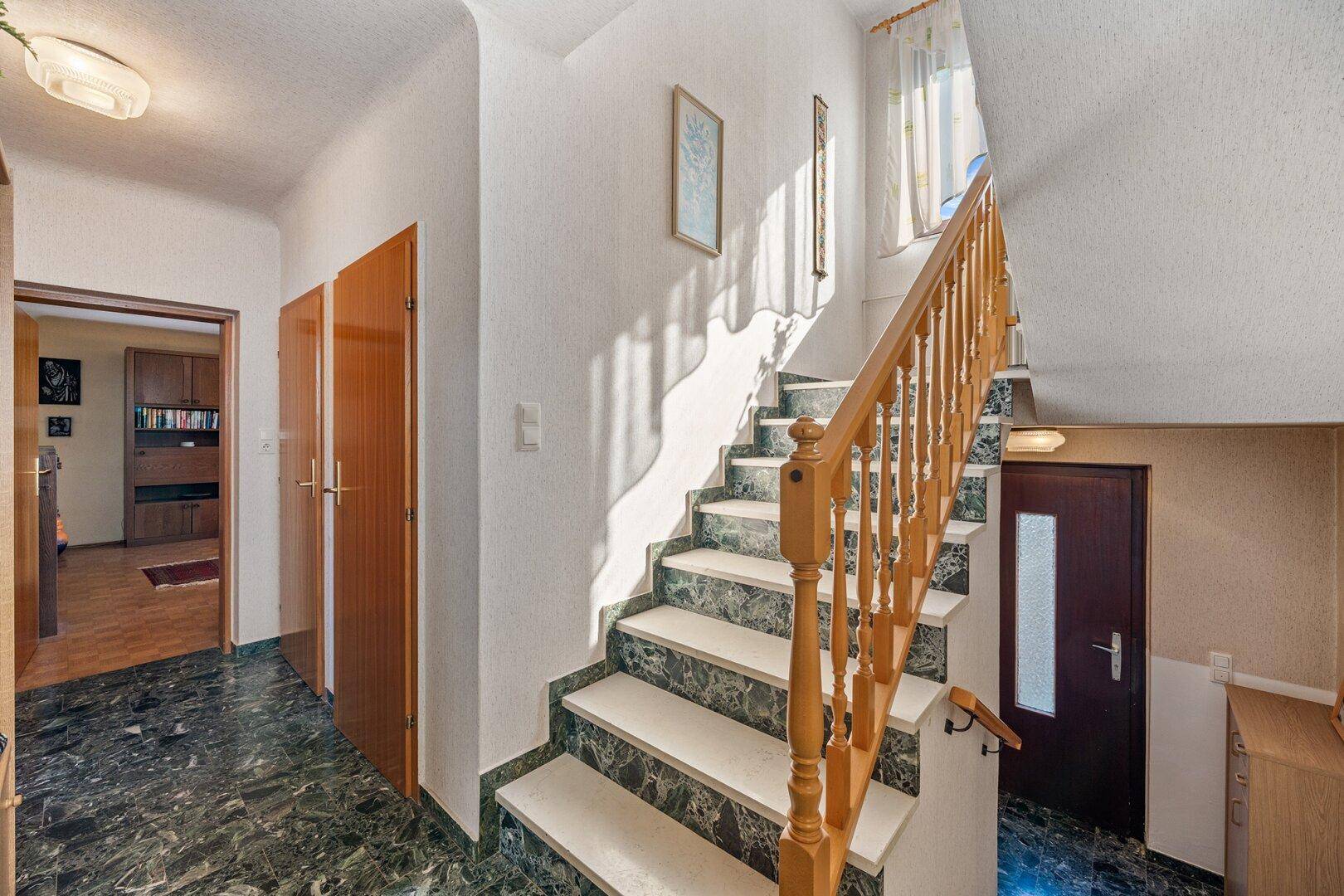 Heller Flur mit Marmorfliesen und Holztreppe, die die Etagen verbindet.