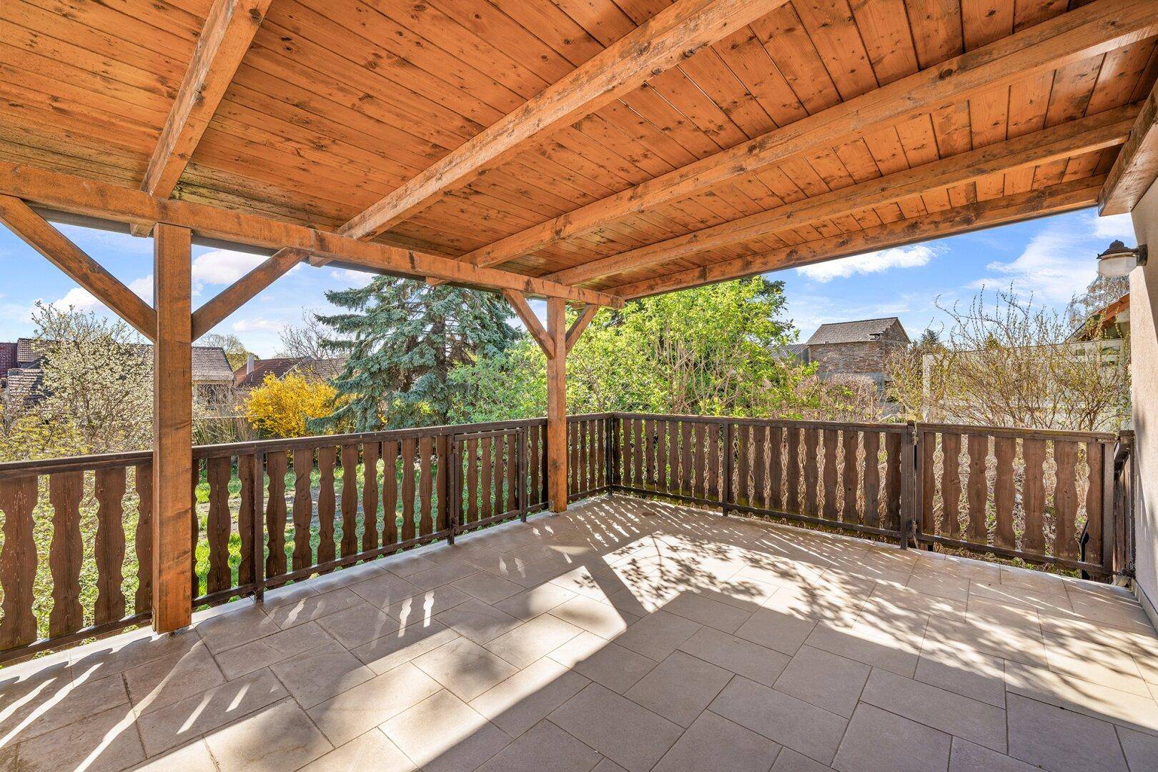 Überdachter Balkon mit Holzbalken und Fliesenboden, ideal für entspannte Stunden im Freien.