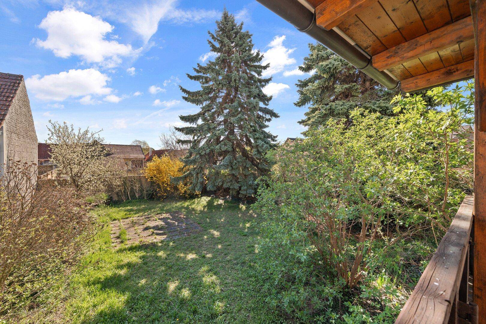 Blick vom Balkon auf den gepflegten Garten mit großen Nadelbäumen und viel Grün.