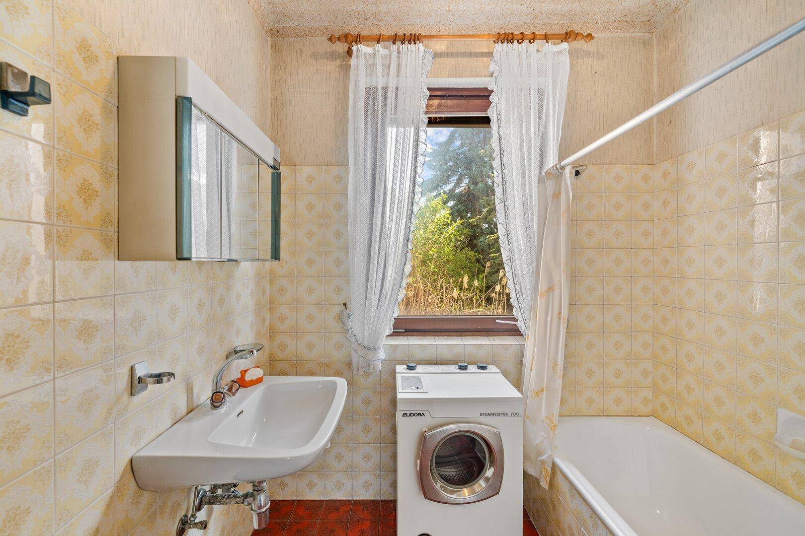 Badezimmer im 80er-Jahre-Stil mit Badewanne, Waschmaschine und Fenster.