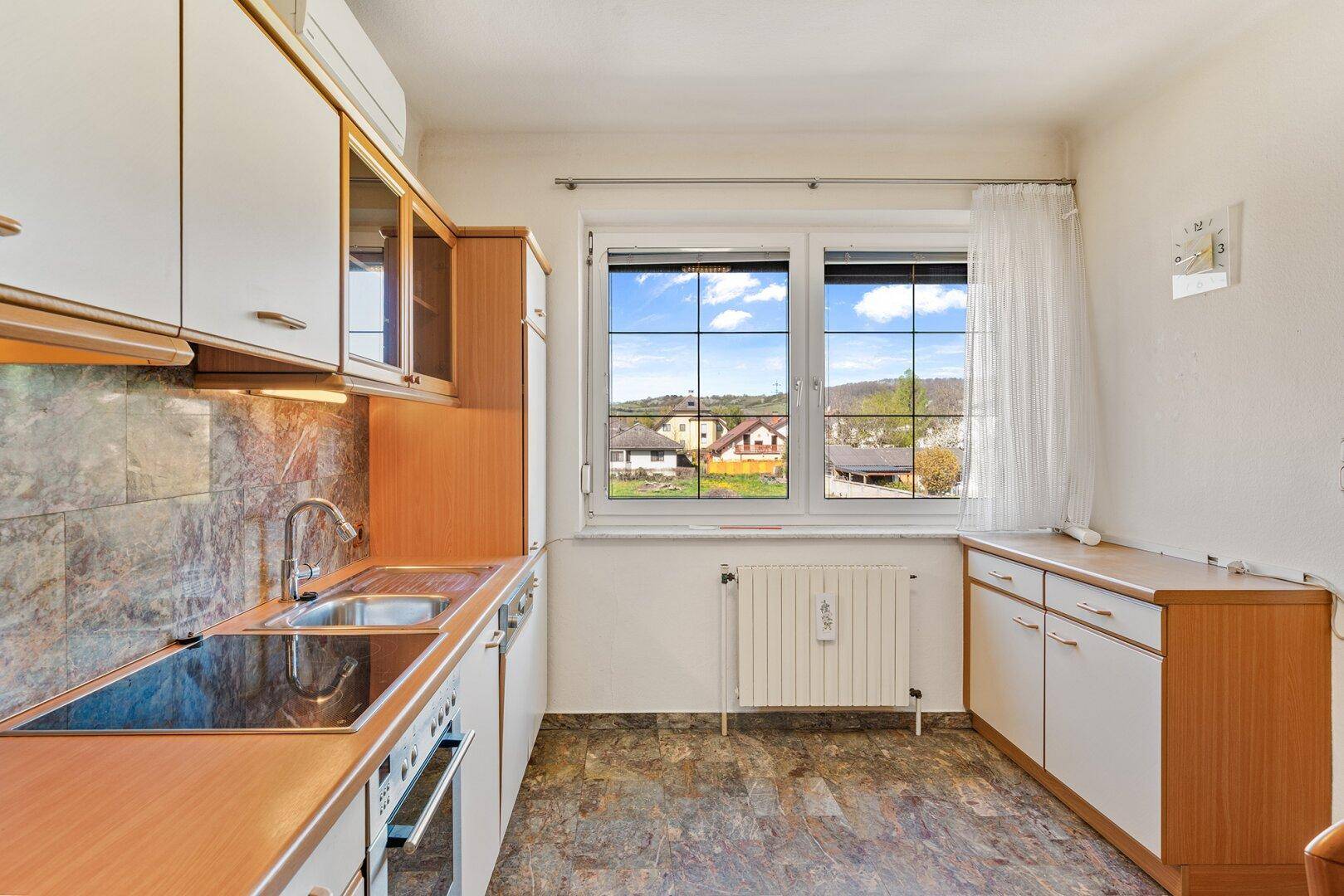 Funktionale Küche mit weißen Schränken, Kochfeld und Fensterblick ins Grüne.