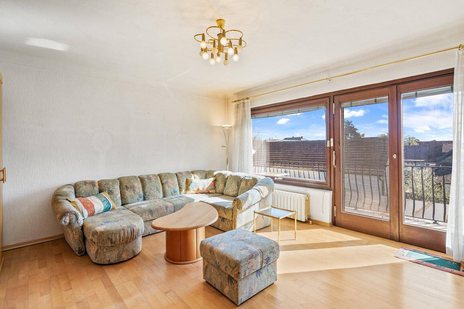 Helles Wohnzimmer mit gemütlicher Sitzecke, Hartholzboden und Zugang zum Balkon.