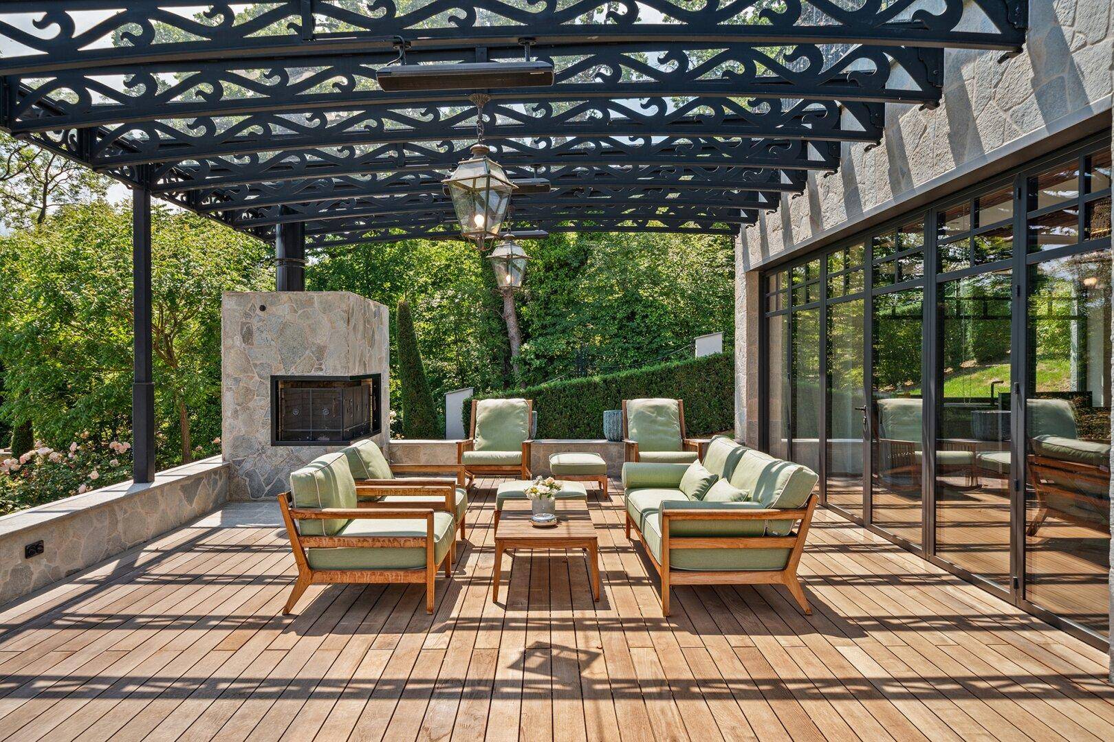 Große Holzterrasse mit schmiedeeiserner Pergola, bequemen Sitzmöbeln und Außenkamin.