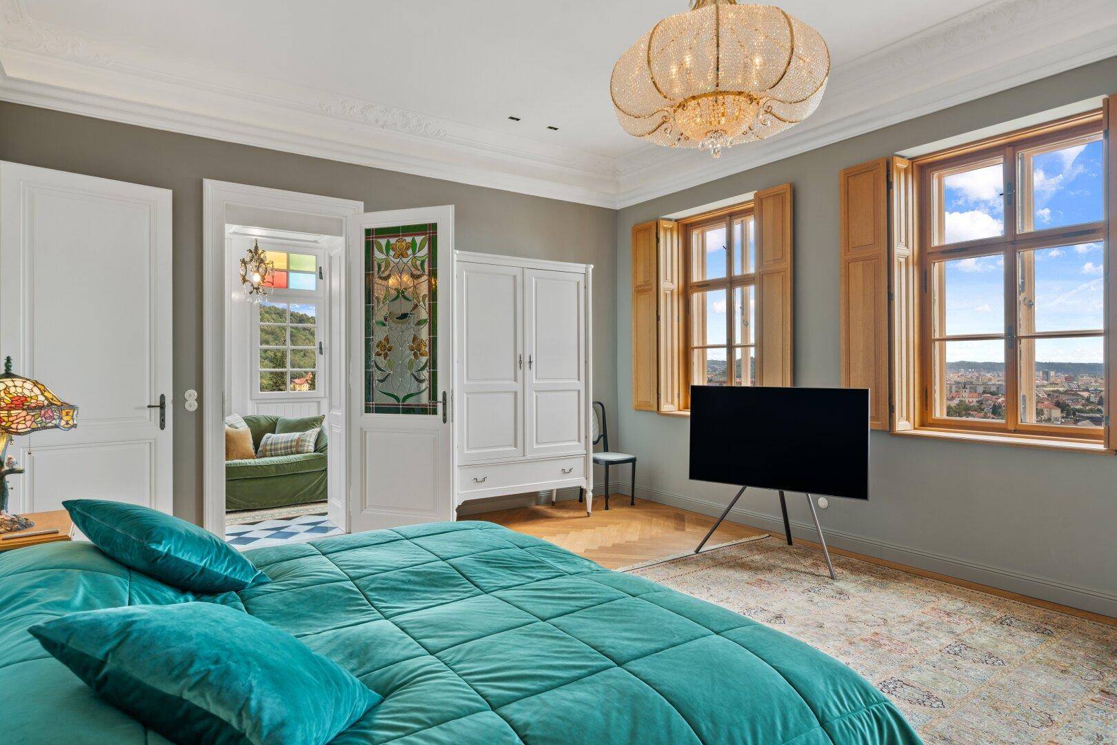 Elegantes Schlafzimmer mit Parkettboden, hohen Decken und Blick auf die Stadt.