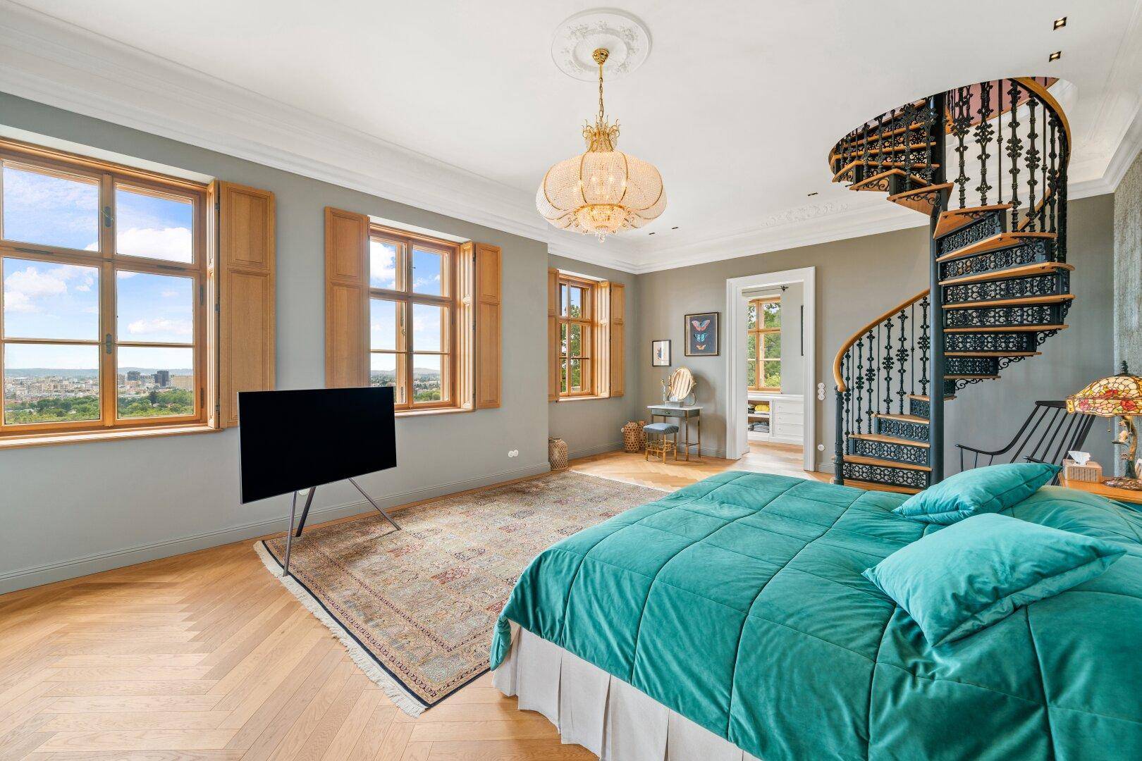 Großes Schlafzimmer mit Parkettboden, hohen Decken und Panoramablick über die Stadt.