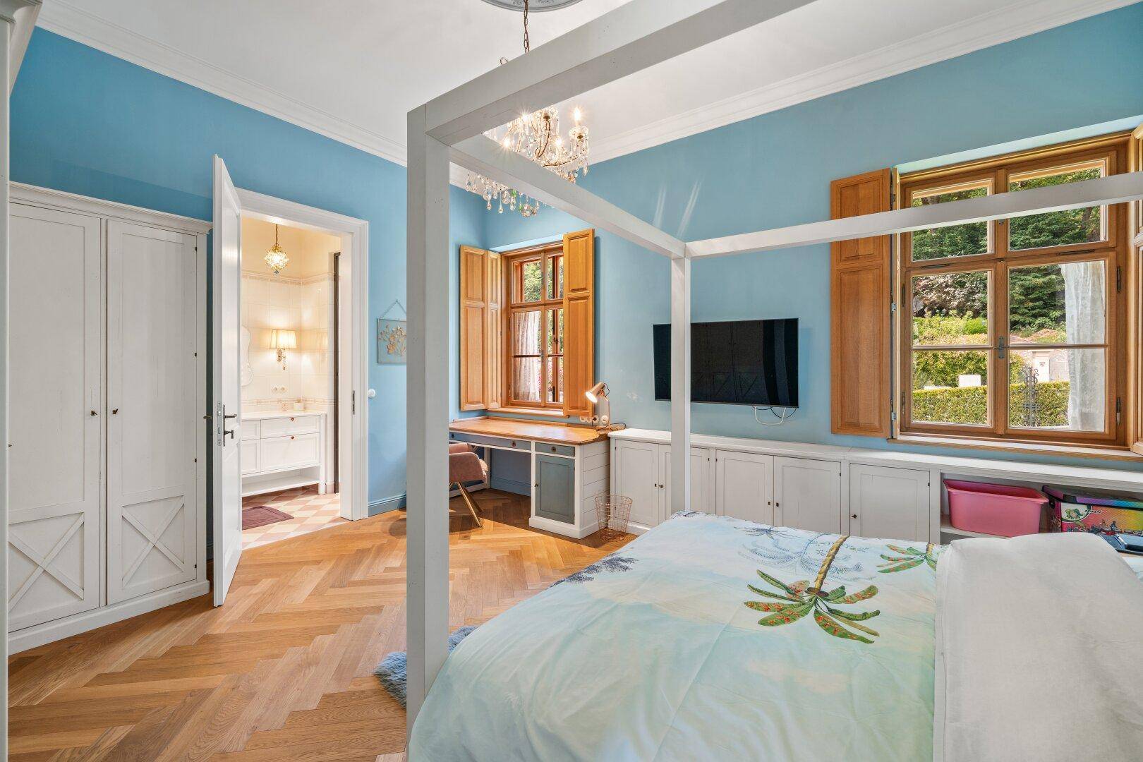 Helles Schlafzimmer mit Himmelbett, Parkettboden und Zugang zu einem angrenzenden Badezimmer.
