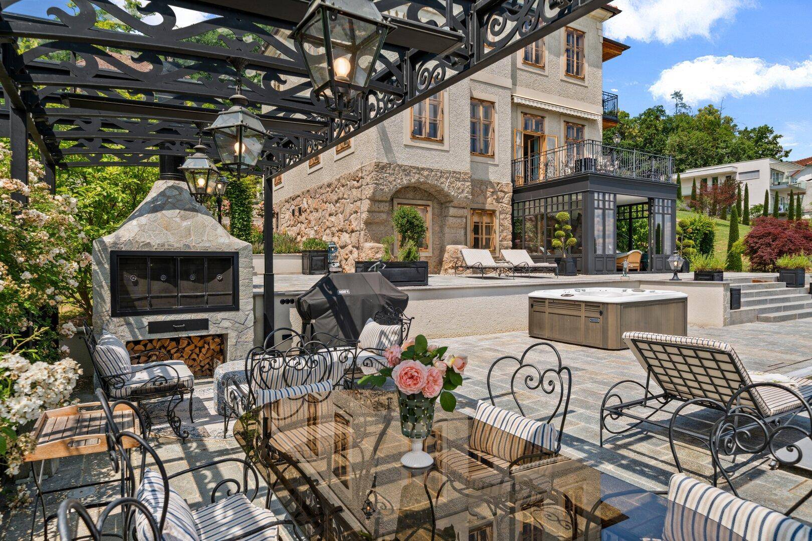 Große Terrasse mit Grillbereich, Essplatz und Blick auf die elegante Villa und den Pool.