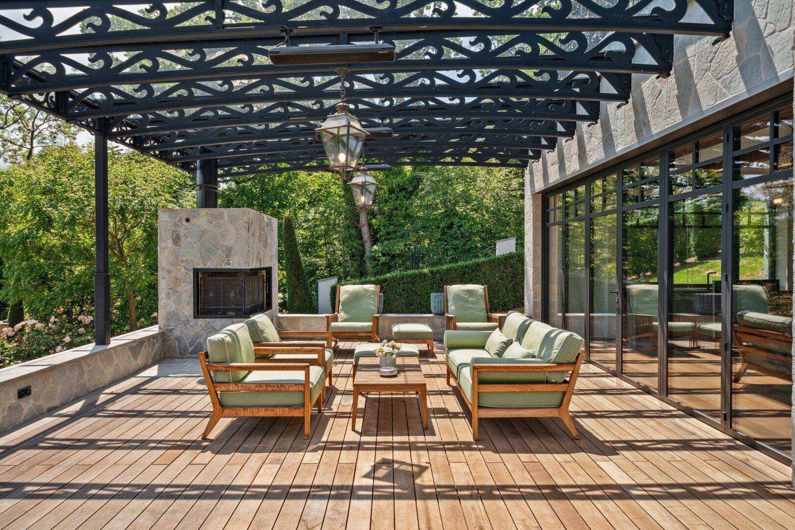 Große Holzterrasse mit schmiedeeiserner Pergola, bequemen Sitzmöbeln und Außenkamin.