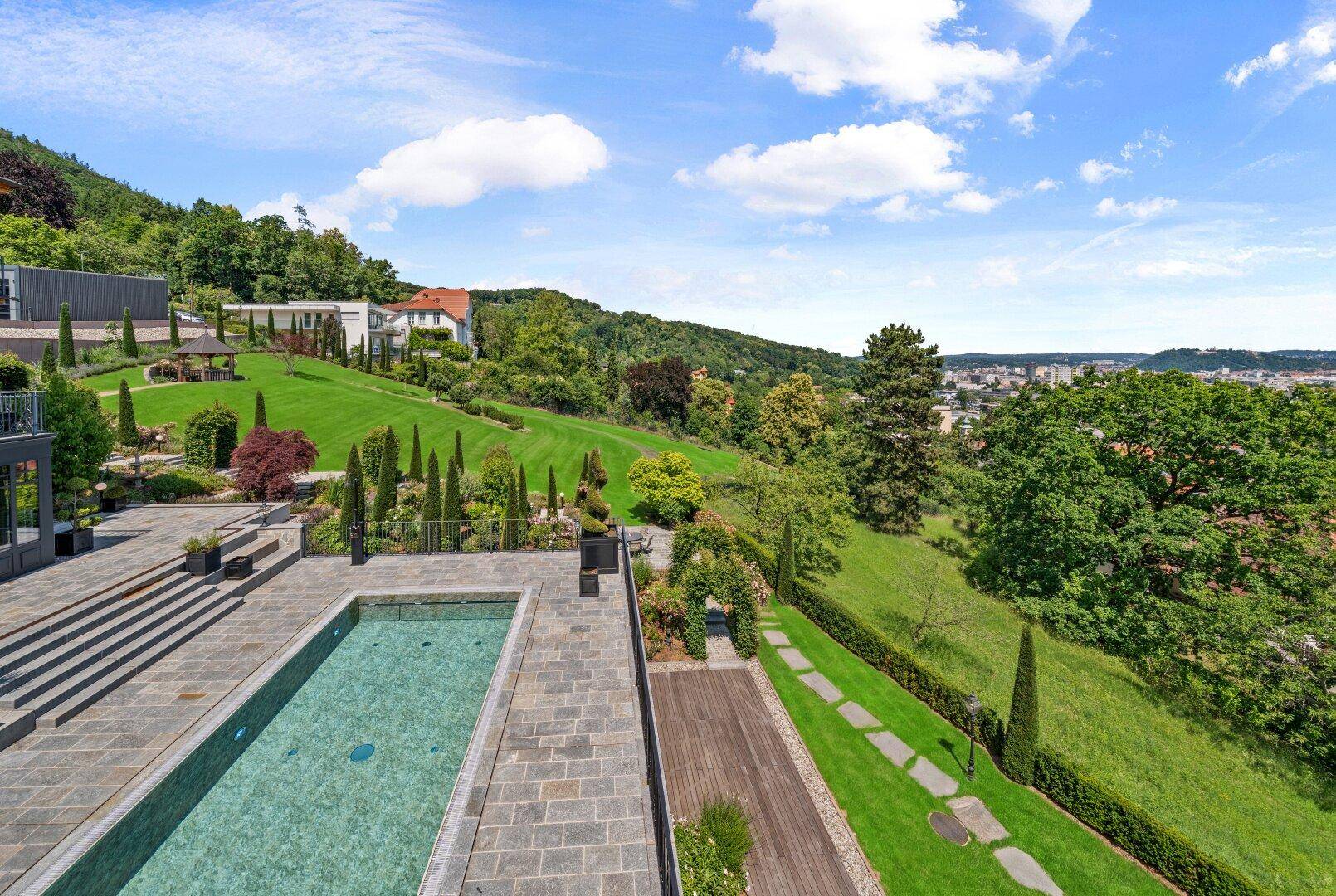 Weitläufiger Gartenbereich mit Pool, Rasenflächen und Blick auf die Stadt und Hügel.