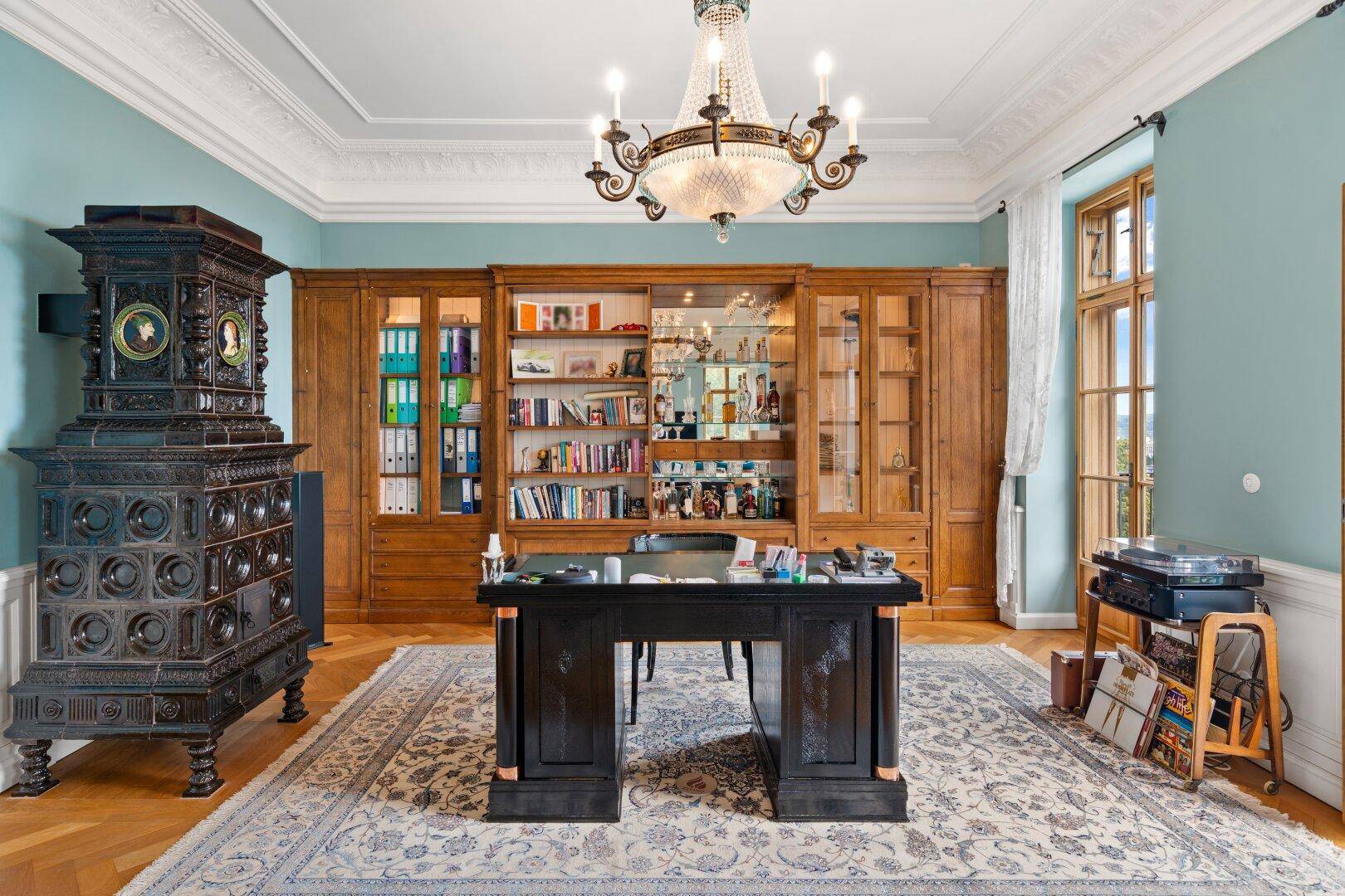 Elegantes Arbeitszimmer mit großem Kachelofen, Holzregalen und einem klassischen Schreibtisch.