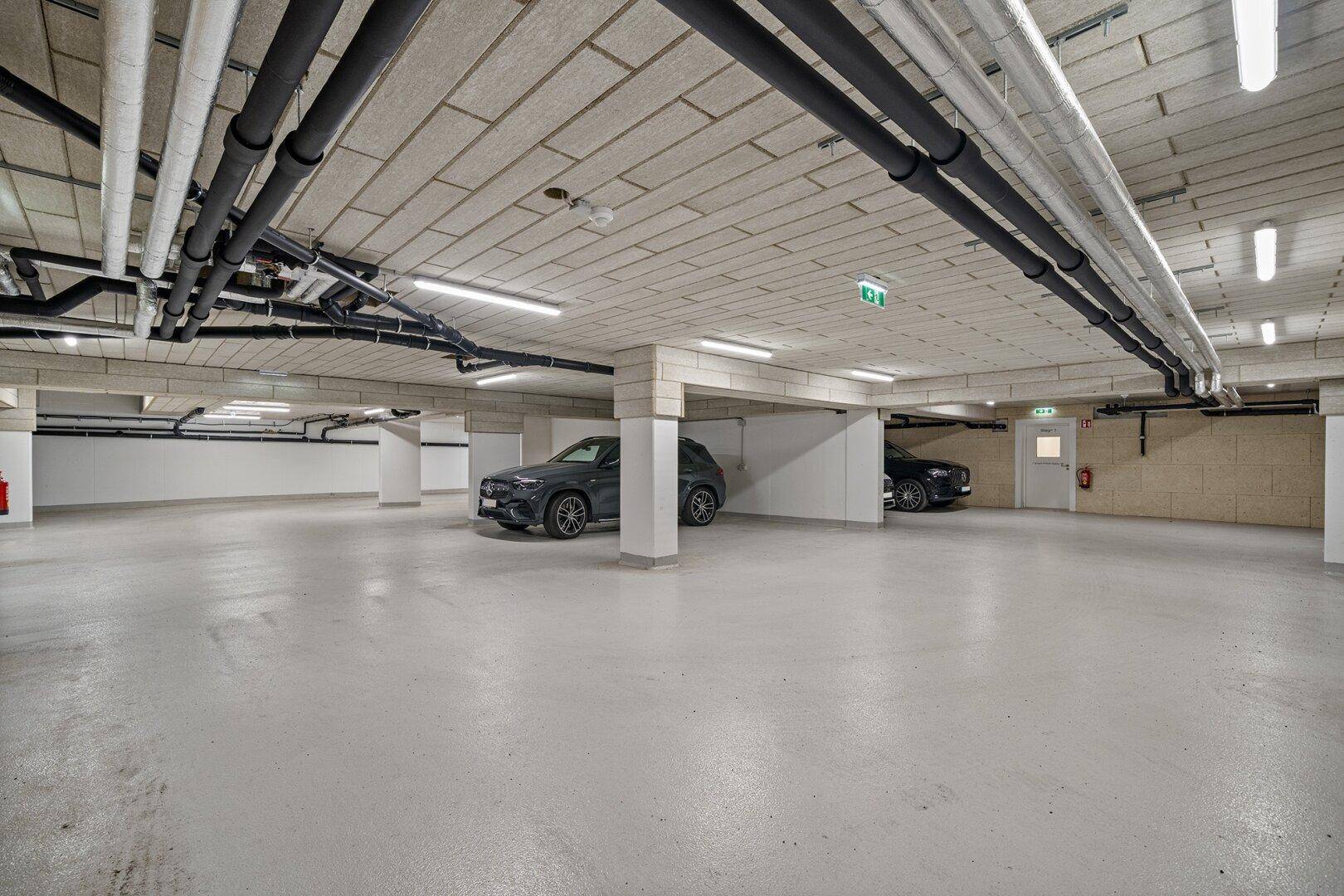 Geräumige Tiefgarage mit Betonboden und sichtbaren Installationen, bietet sichere Stellplätze.