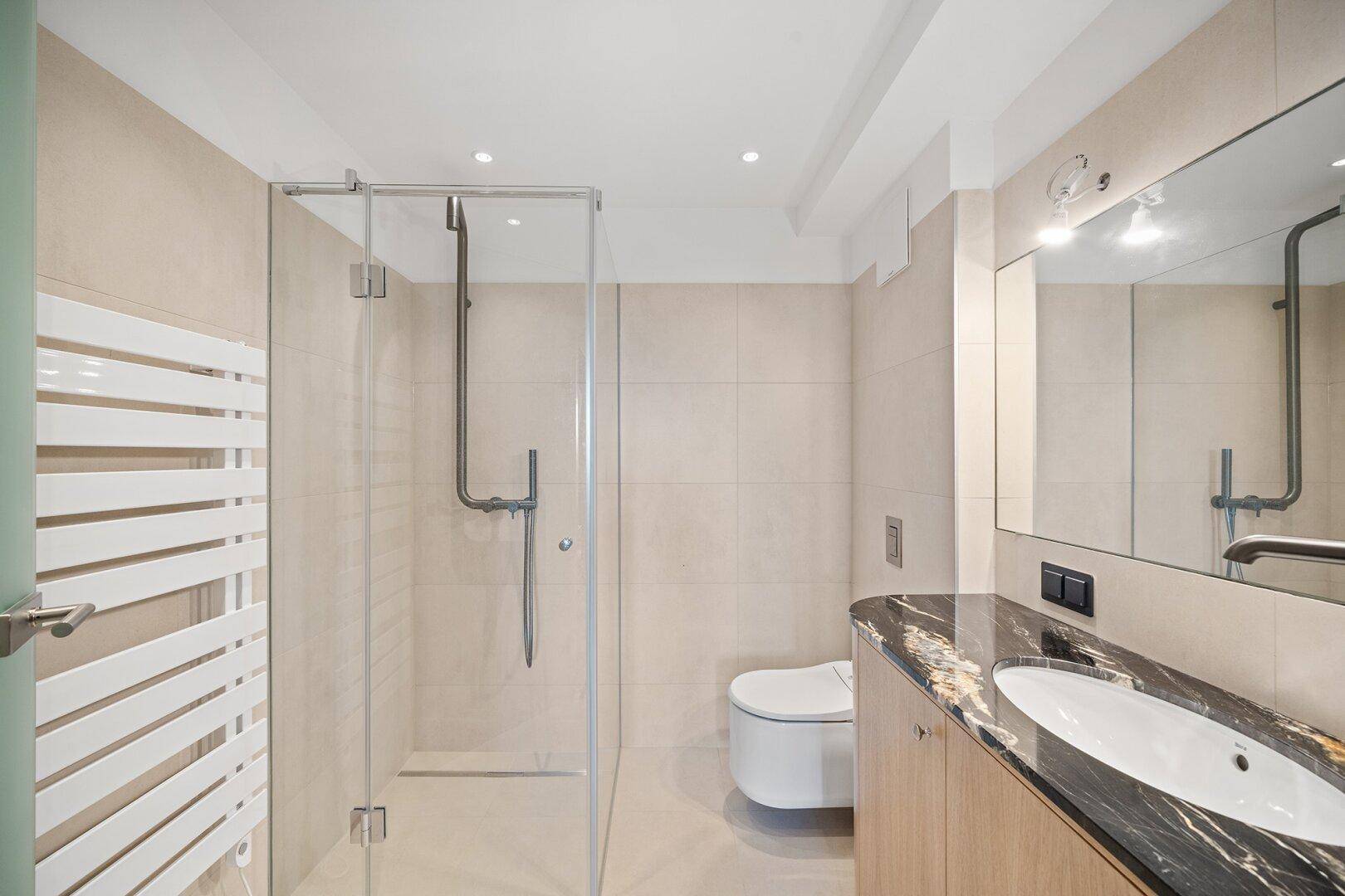 Modernes Badezimmer mit begehbarer Dusche, Marmorwaschtisch und beheiztem Handtuchhalter.