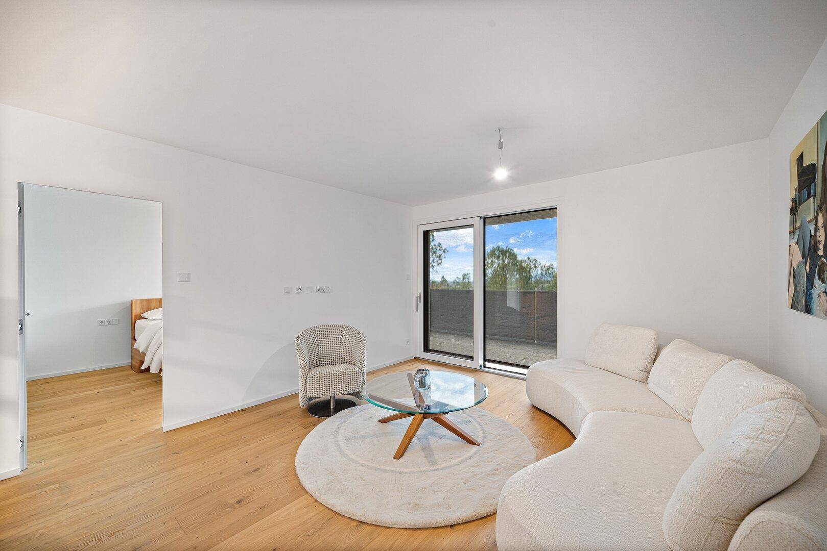 Gemütliches Wohnzimmer mit weißem Sofa und Holzboden, angrenzend an ein Schlafzimmer.