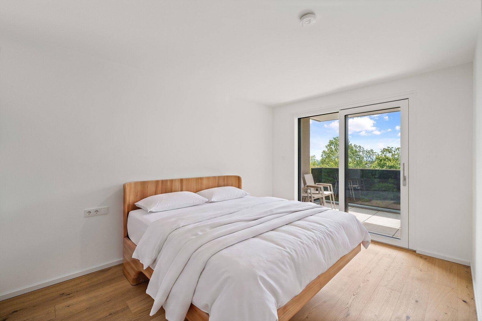 Helles Schlafzimmer mit Holzbett, Holzboden und direktem Zugang zu einem privaten Balkon.