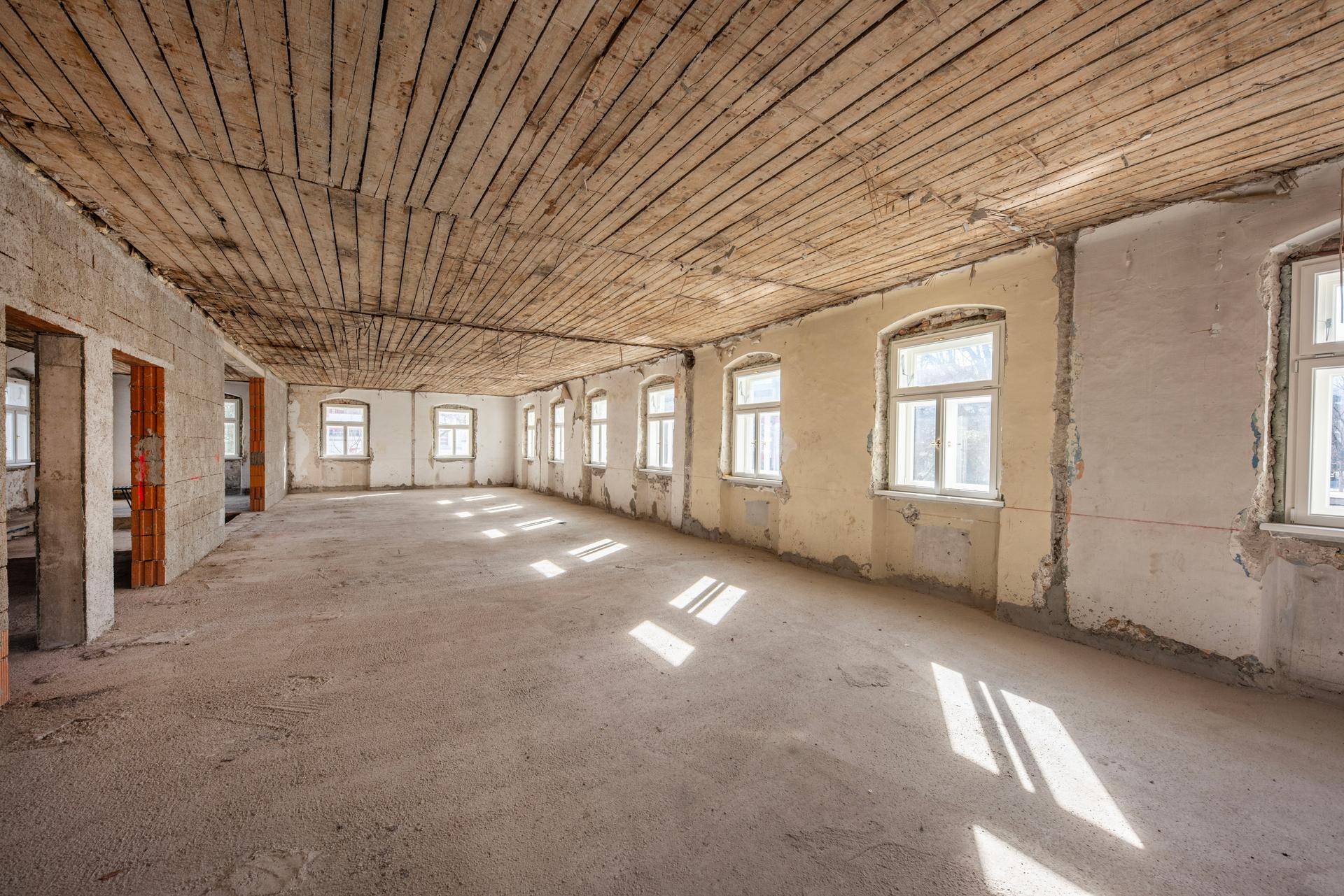 Unfertiger Raum mit Holzdeckenverkleidung und vielen Fenstern, bereit für den Innenausbau.
