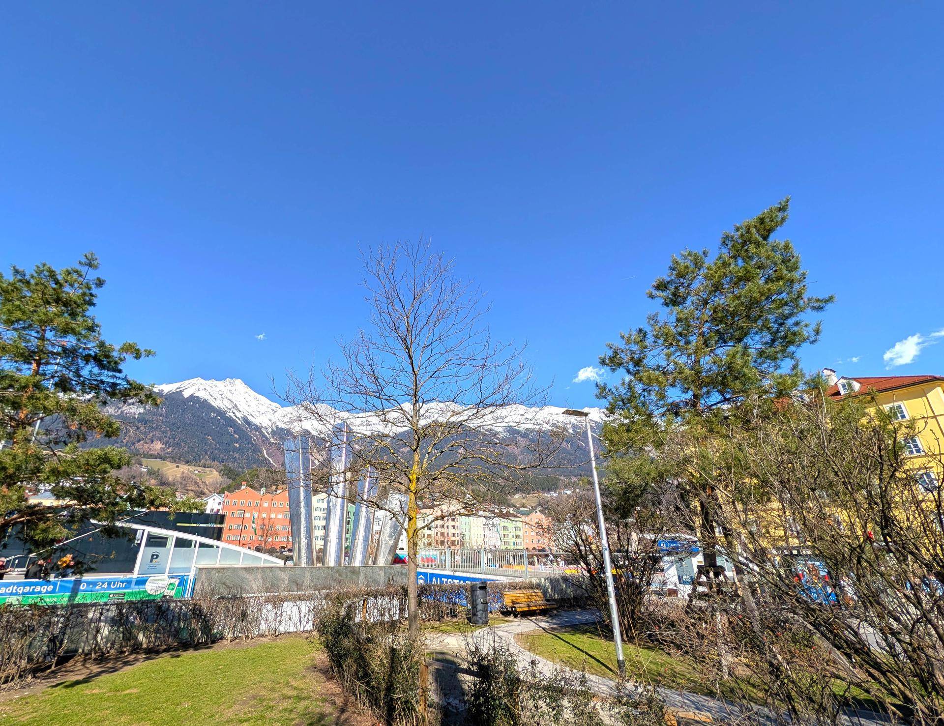 Grüne Umgebung mit Bäumen, einer Straße und einem beeindruckenden Blick auf schneebedeckte Berge.