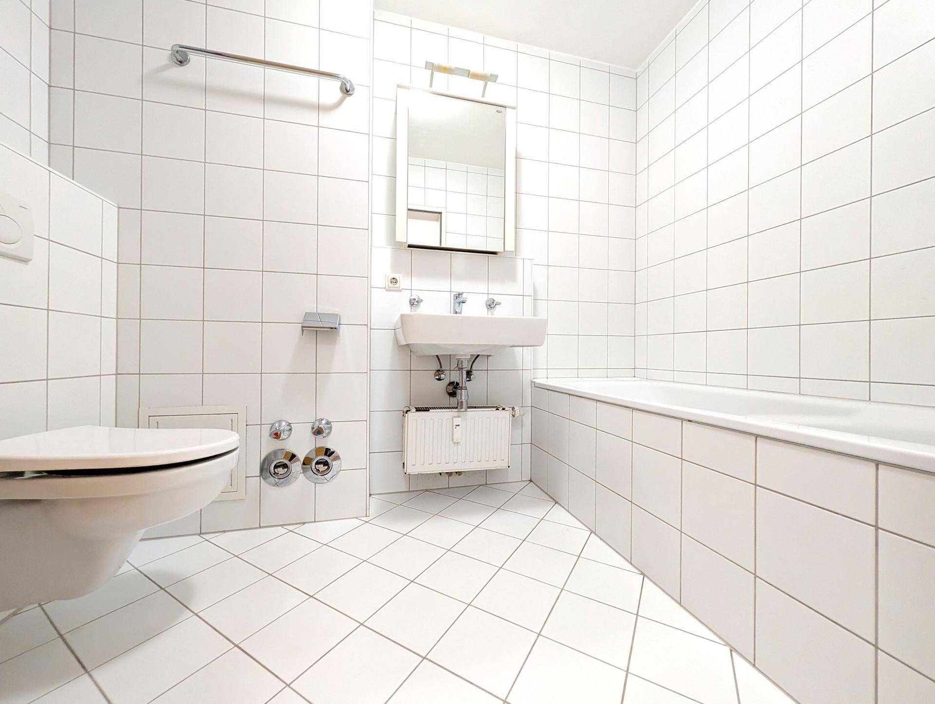 Helles Badezimmer mit weißen Fliesen, Badewanne, Toilette und Waschbecken in gutem Zustand.