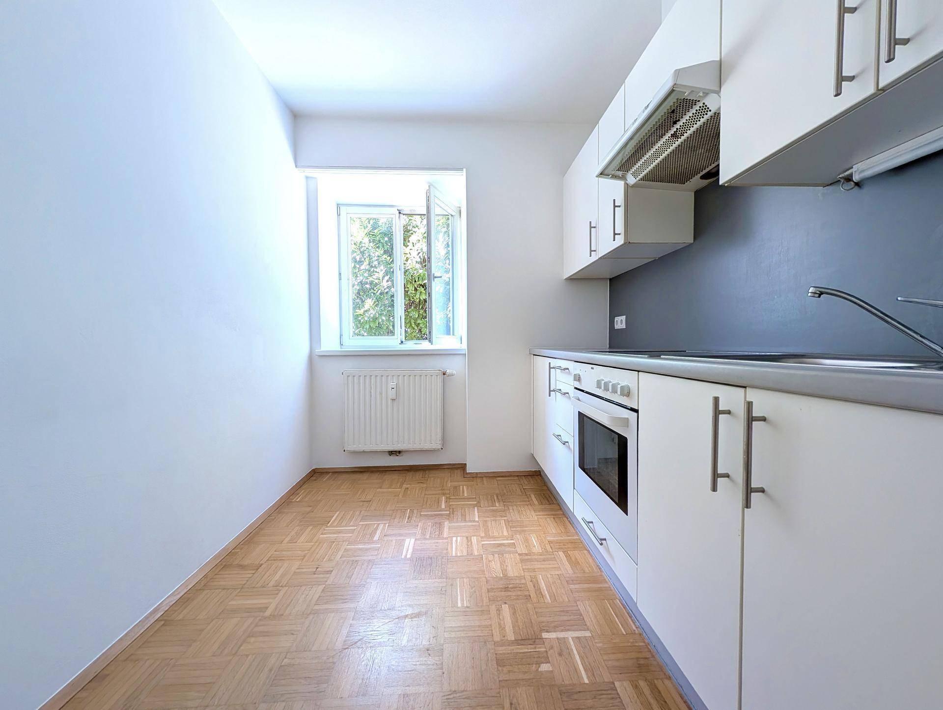 Funktionale Küche mit weißen Schränken, integrierten Geräten und einem Fenster für Tageslicht.