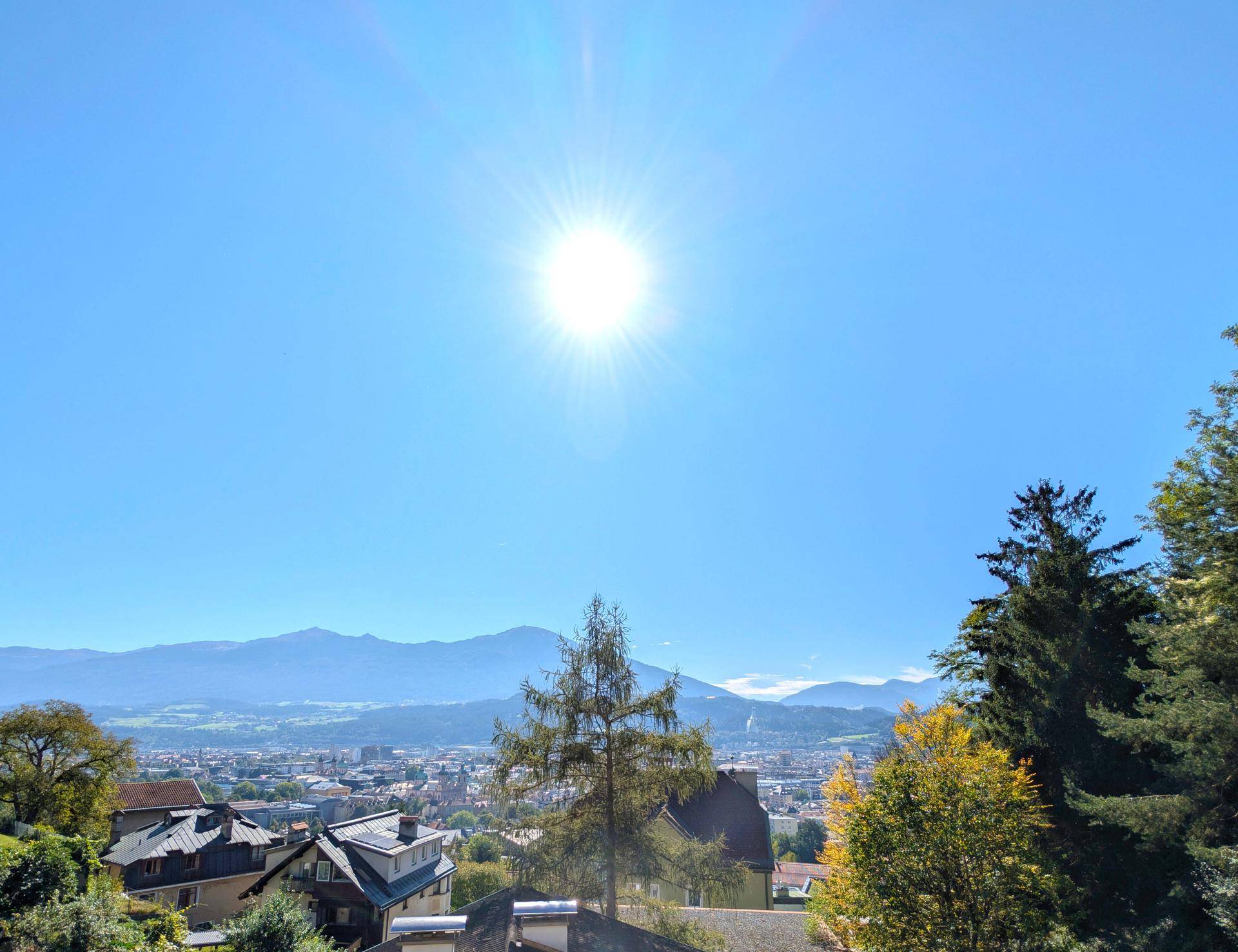 Sonniger Tag mit weitem Blick über eine Stadt und die umliegende Berglandschaft.