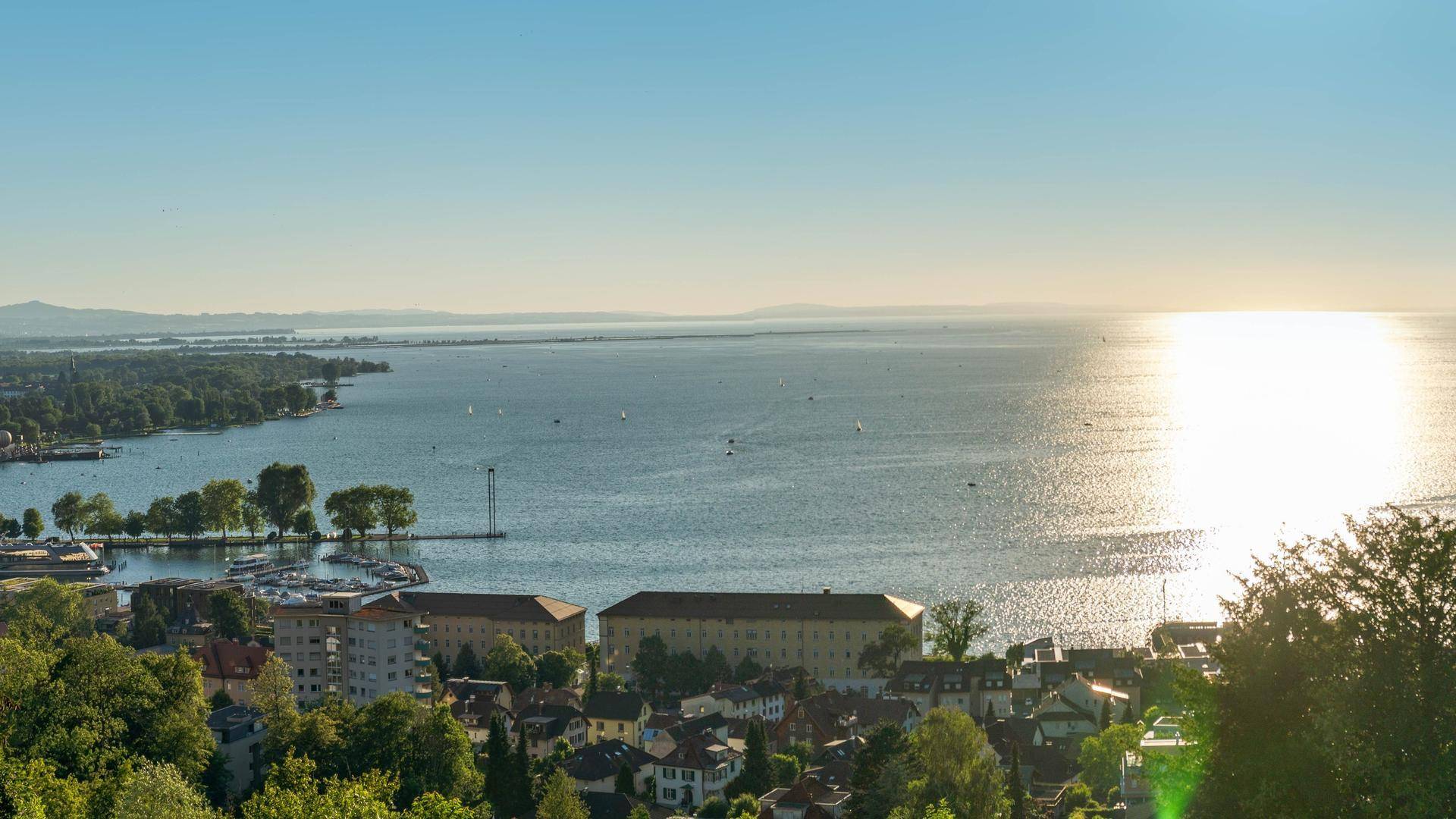 Sonniger Panoramablick auf den See und die Stadt mit ihren Hafenanlagen und grünen Ufern.
