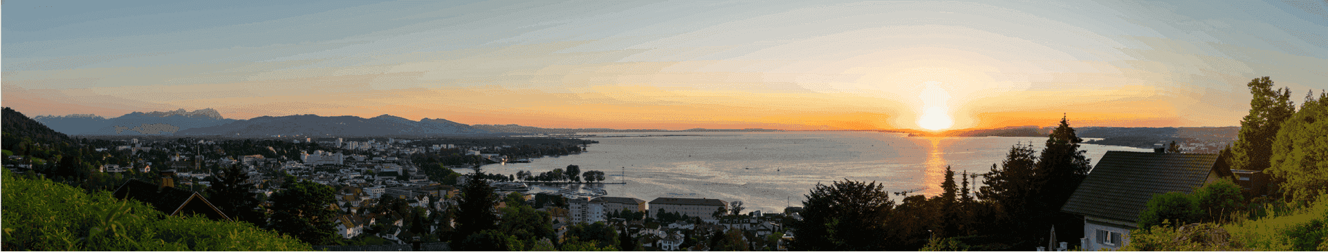 Malerischer Sonnenuntergang über dem See mit Blick auf die Stadt und die ferne Bergkette.