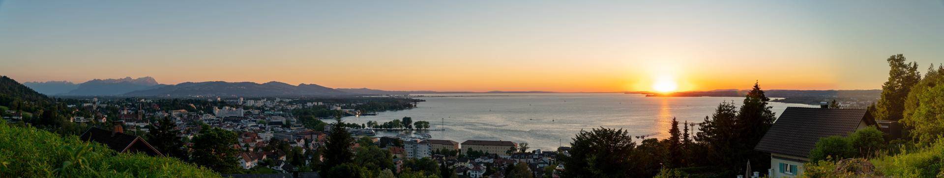 Panoramablick auf einen See, eine Stadt und Berge bei Sonnenuntergang mit warmen Farben.