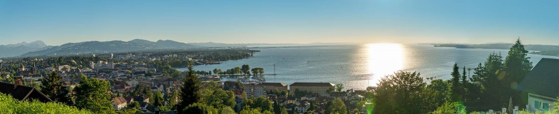 Panoramablick auf eine Stadt am See mit Bergen im Hintergrund bei Sonnenuntergang.