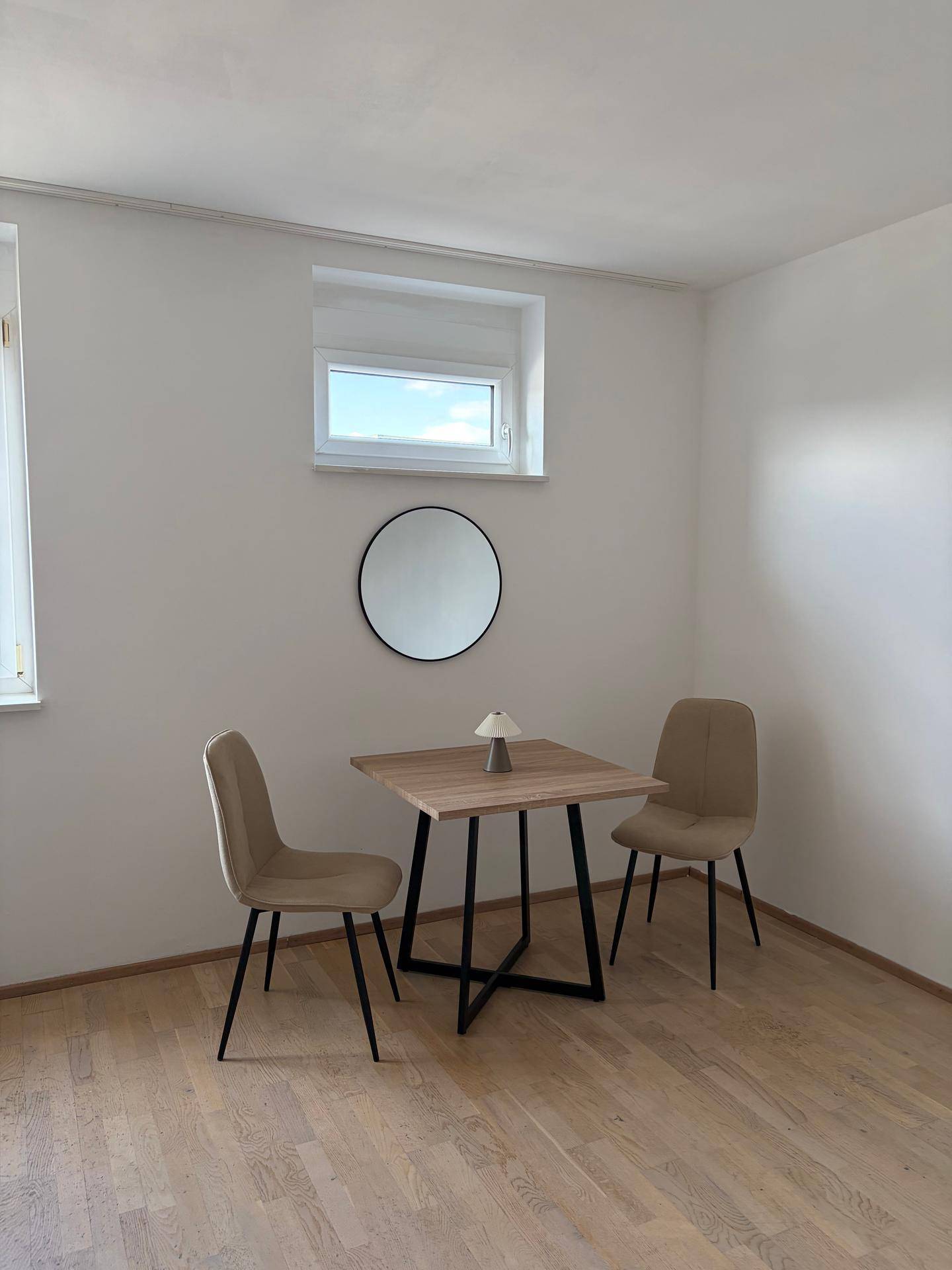 Heller Essbereich mit modernem Holztisch, zwei beigen Stühlen und einem runden Wandspiegel.