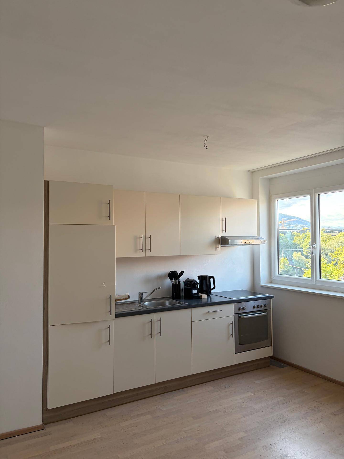 Funktionale Küchenzeile mit hellen Schränken, integriertem Ofen und Fenster mit Ausblick.