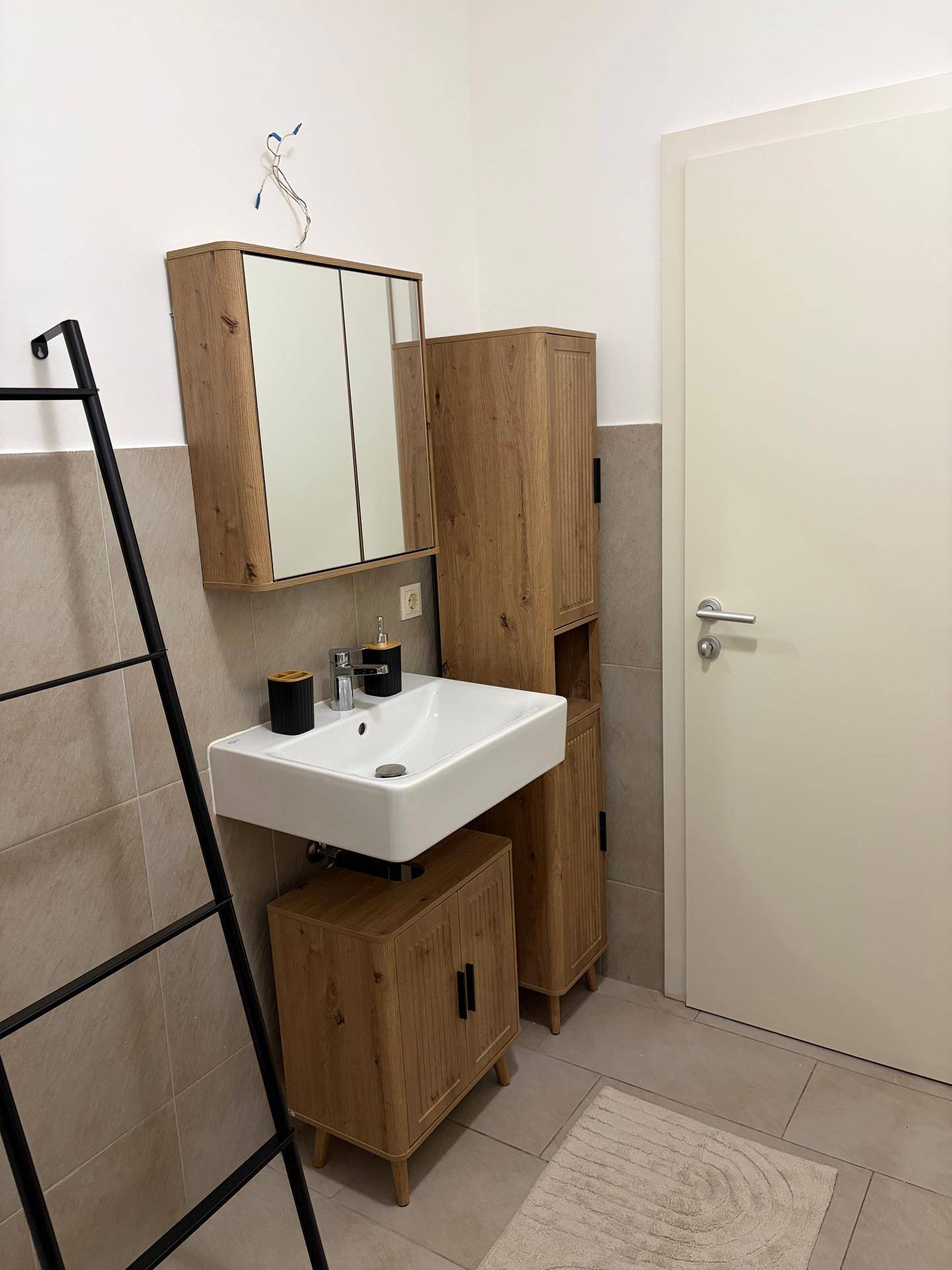 Badezimmer mit modernem Waschbecken, Spiegelschrank und passenden Holzschränken.