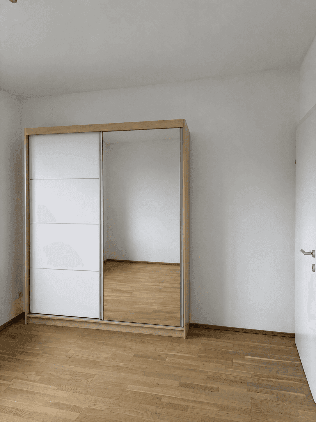 Helles Zimmer mit großem Kleiderschrank mit Spiegeltüren und Holzfußboden.
