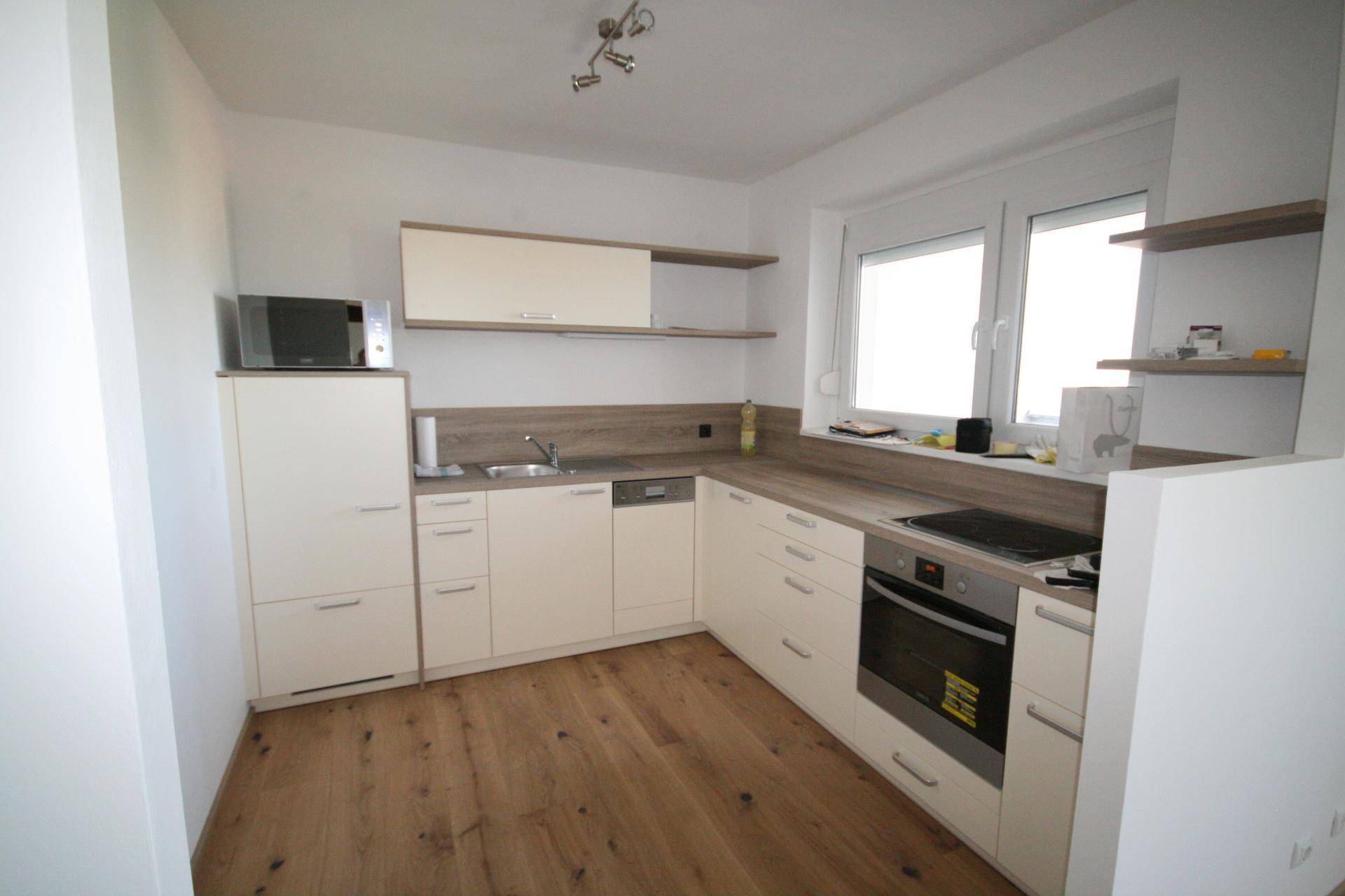 Moderne Einbauküche mit hellen Schränken, Holz-Arbeitsplatten und integrierten Geräten.