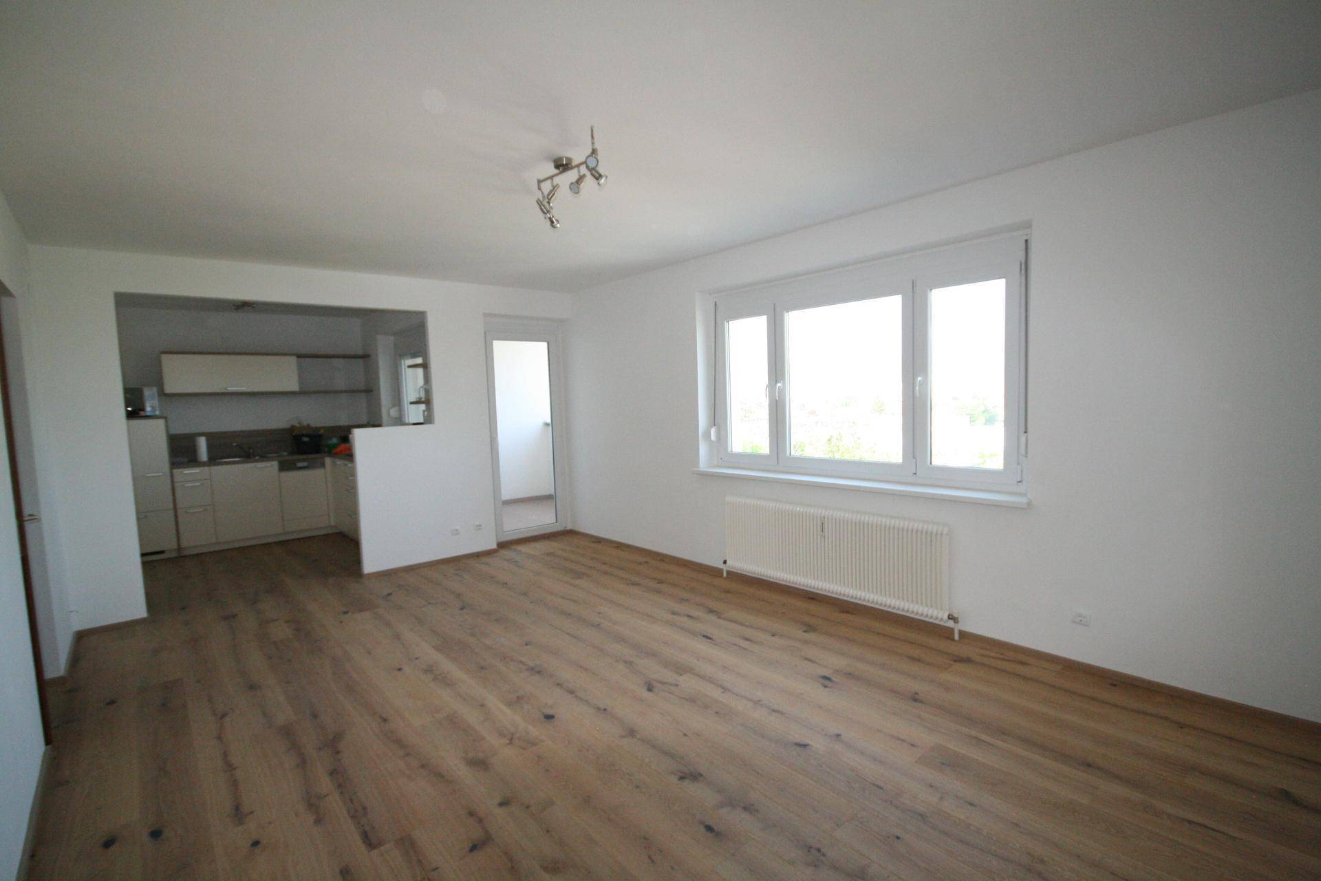 Heller Wohnbereich mit neuem Holzboden, großen Fenstern und offenem Zugang zur Küche.