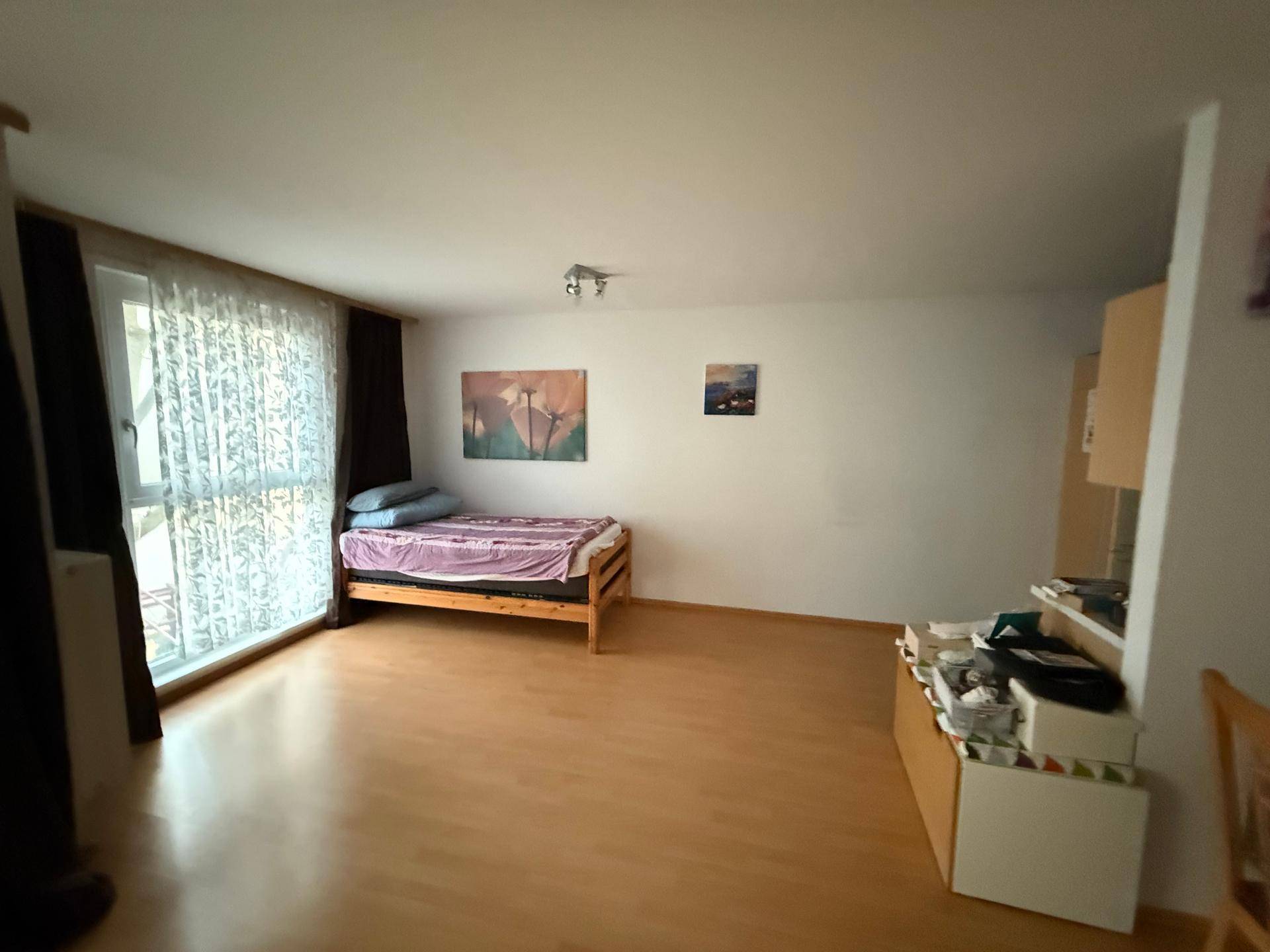 Heller Wohnraum mit Laminatboden, einem Einzelbett und praktischen Staumöbeln.