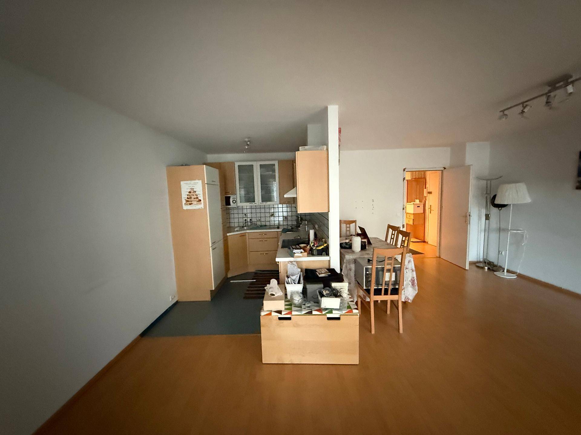 Offener Wohnbereich mit integrierter Küche, Essplatz und hellem Laminatboden.