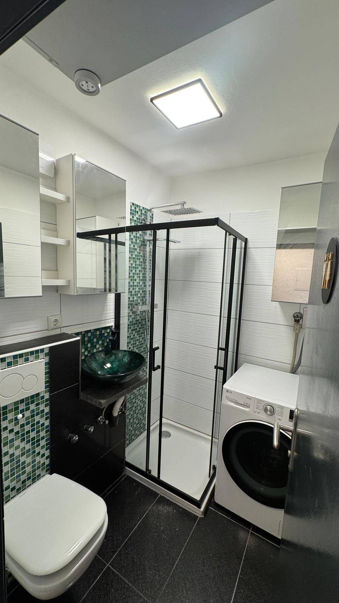 Modernes Badezimmer mit Duschkabine, WC, grünem Waschbecken und Waschmaschine.
