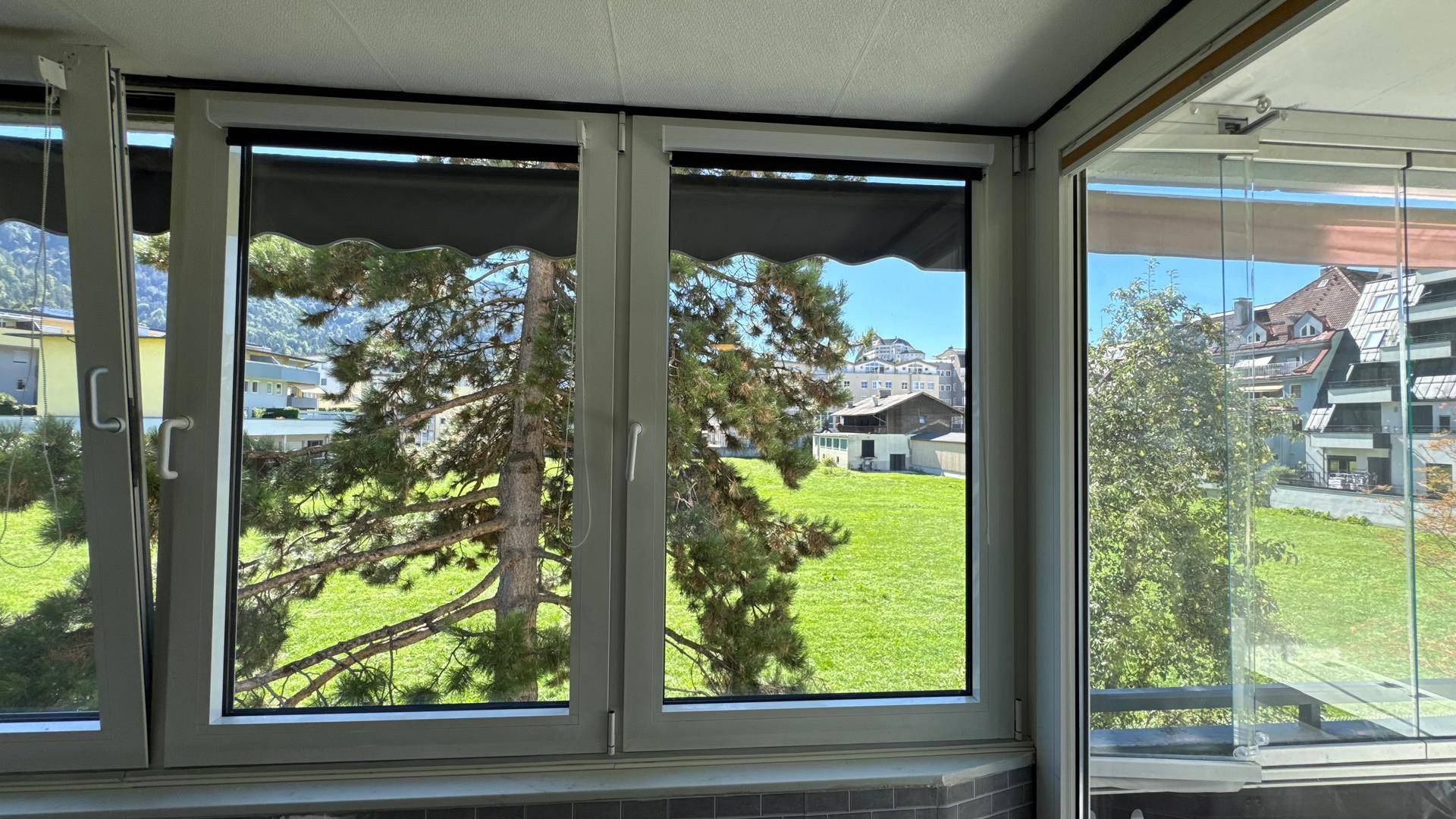 Heller Wohnbereich mit großen Fenstern und Blick auf einen Baum und die Umgebung.