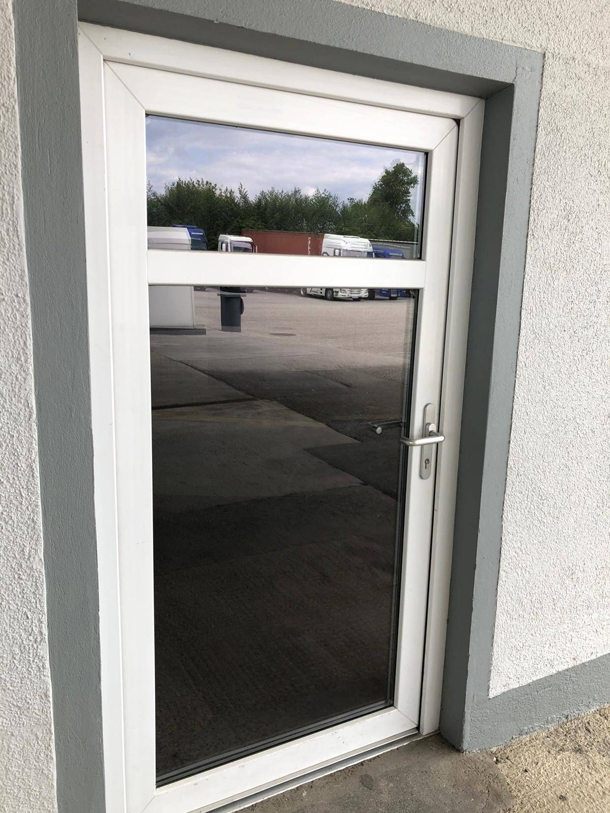 Weiße Eingangstür mit großer Glasfläche, die den Außenbereich des Gewerbeparks widerspiegelt.