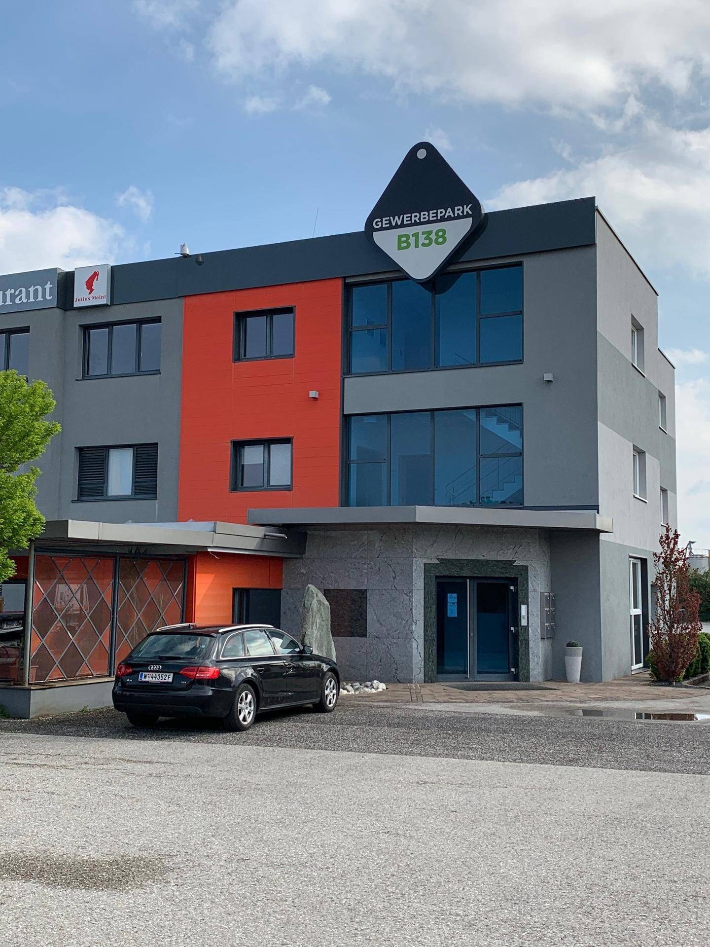 Moderne Fassade eines Gewerbeparks mit markanten orangefarbenen Akzenten und großen Fenstern am Eingangsbereich.