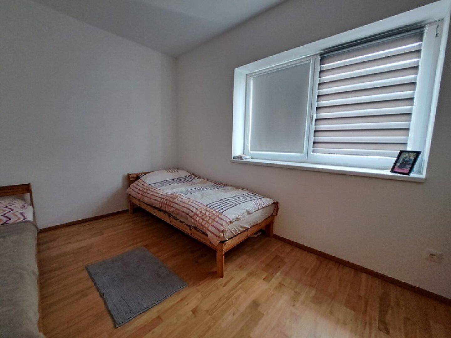 Gemütliches Schlafzimmer mit Einzelbett, Holzfußboden und Fenster für natürliches Licht.
