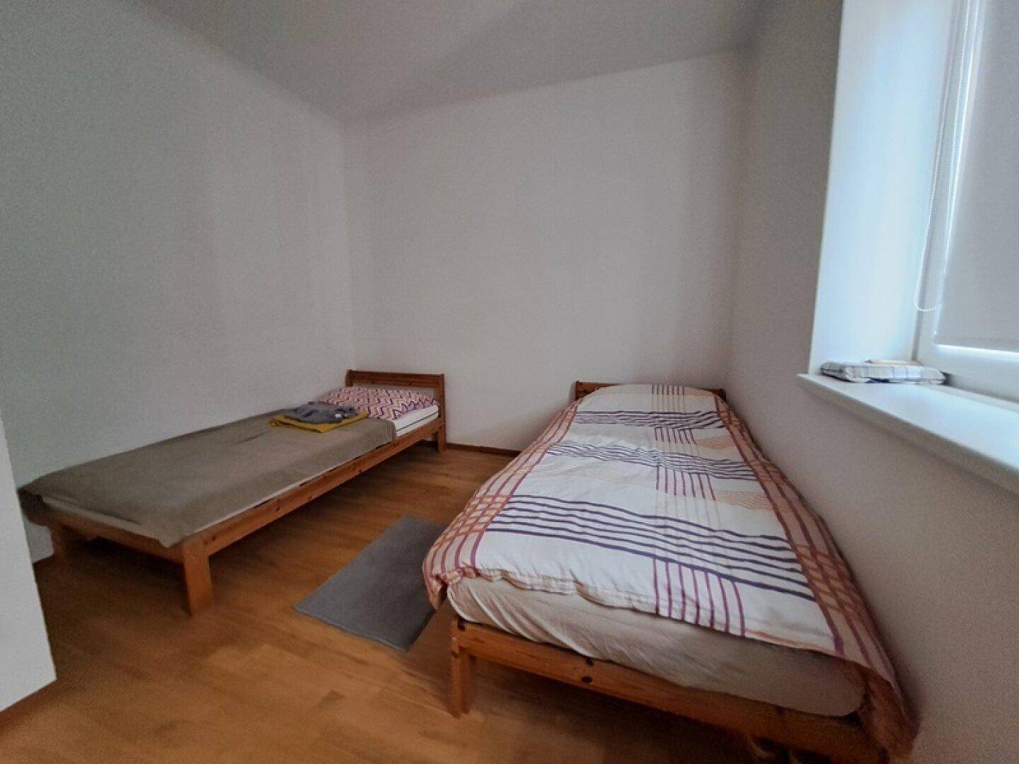 Helles Schlafzimmer mit zwei Einzelbetten und Holzrahmen, ideal als Gäste- oder Kinderzimmer.