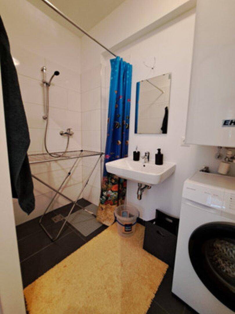 Modernes Badezimmer mit Dusche, Waschbecken und Waschmaschine, praktisch und funktional eingerichtet.