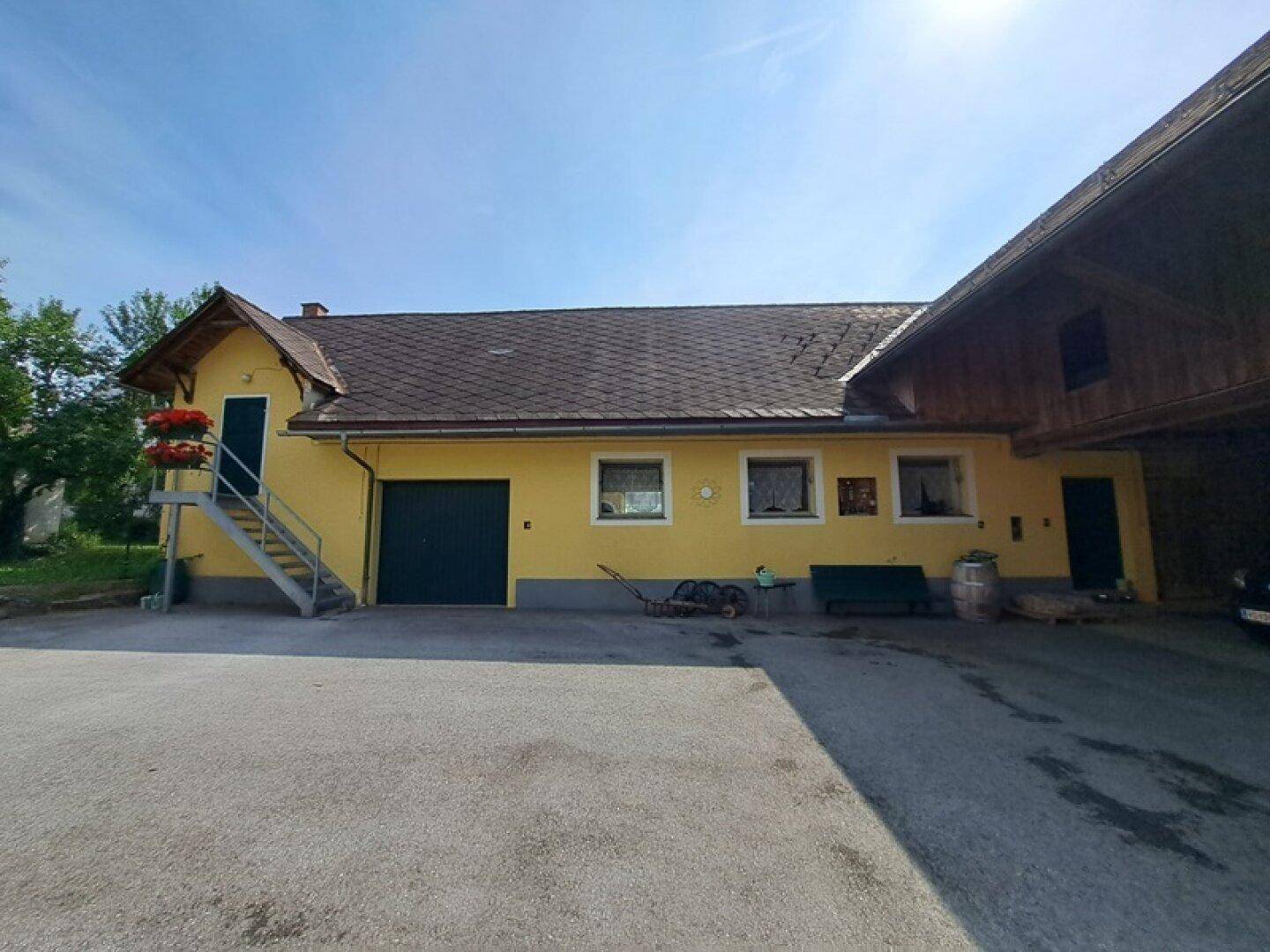 Gelbes Nebengebäude mit dunklem Dach, Garagentor und Außentreppe auf dem Grundstück.