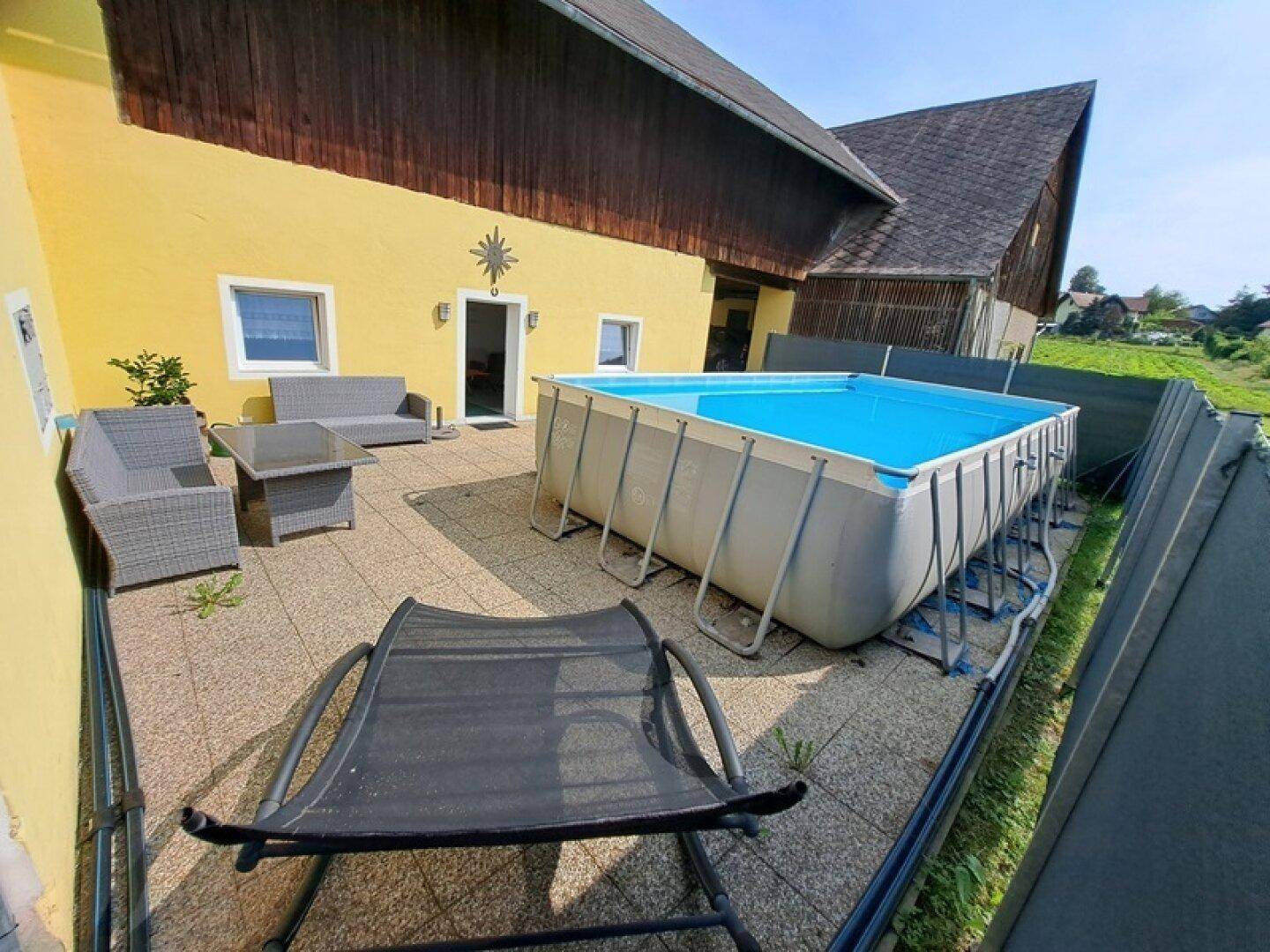 Gemütliche Terrasse mit Aufstellpool und Outdoor-Sitzgelegenheiten neben dem Gebäude.
