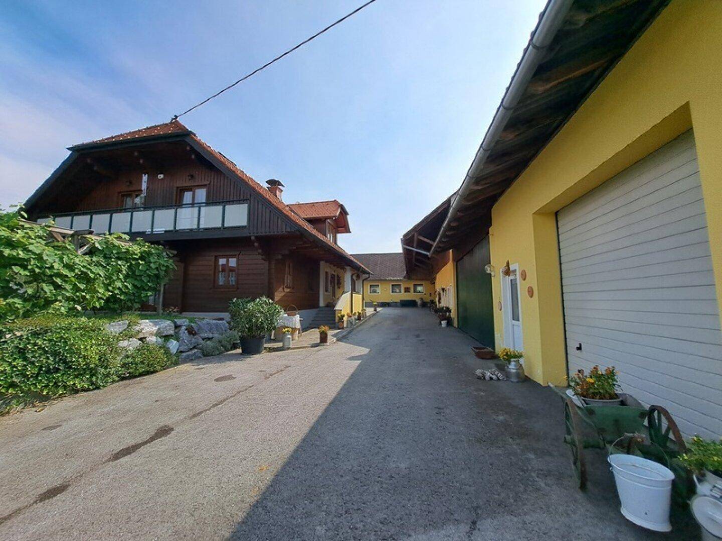 Zufahrt zwischen zwei Gebäuden, einem Holzhaus und einem gelben Nebengebäude.