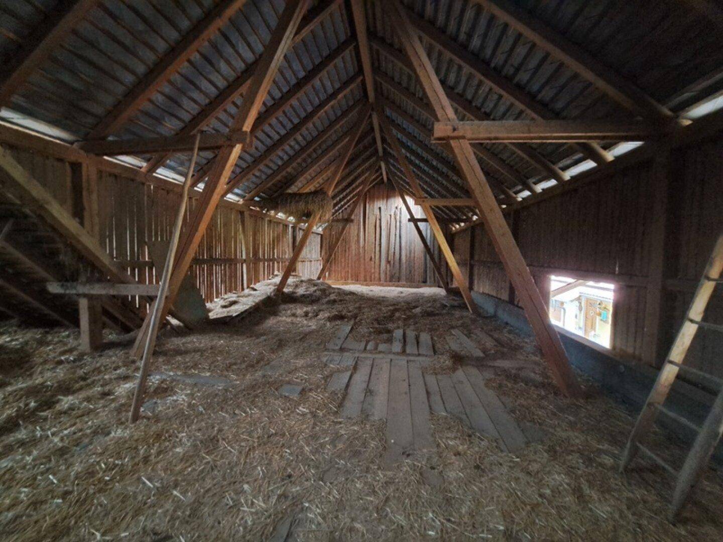 Geräumiger Dachboden mit sichtbaren Holzbalken und Stroh auf dem Boden.